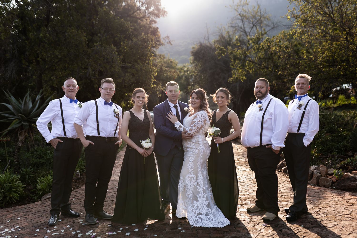 Wedding party in black and white attire poses together at outdoor venue.