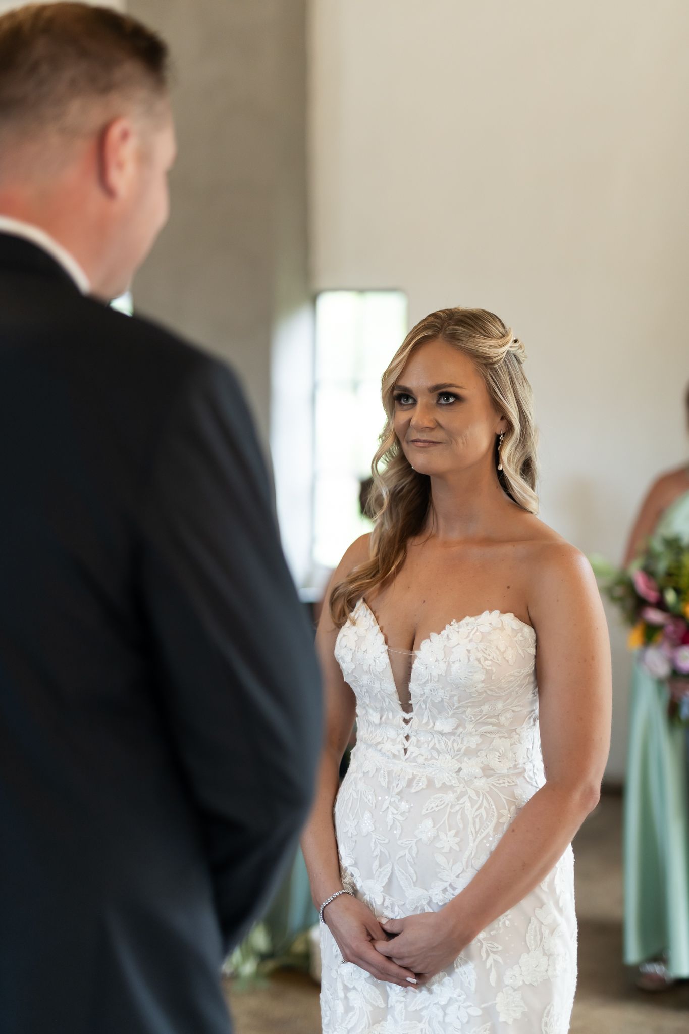 A bride in a strapless lace wedding gown stands during the ceremony.