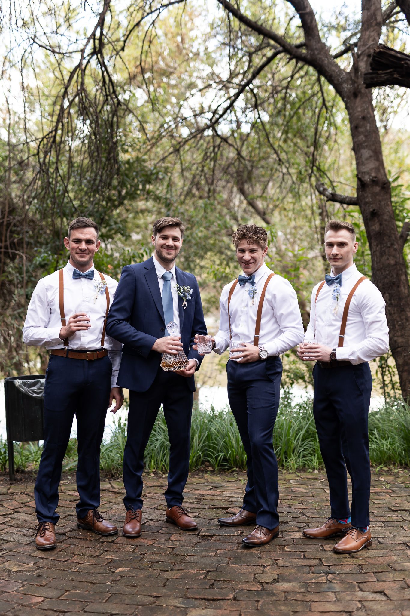 Four groomsmen in coordinated navy and white attire posing on brick path.