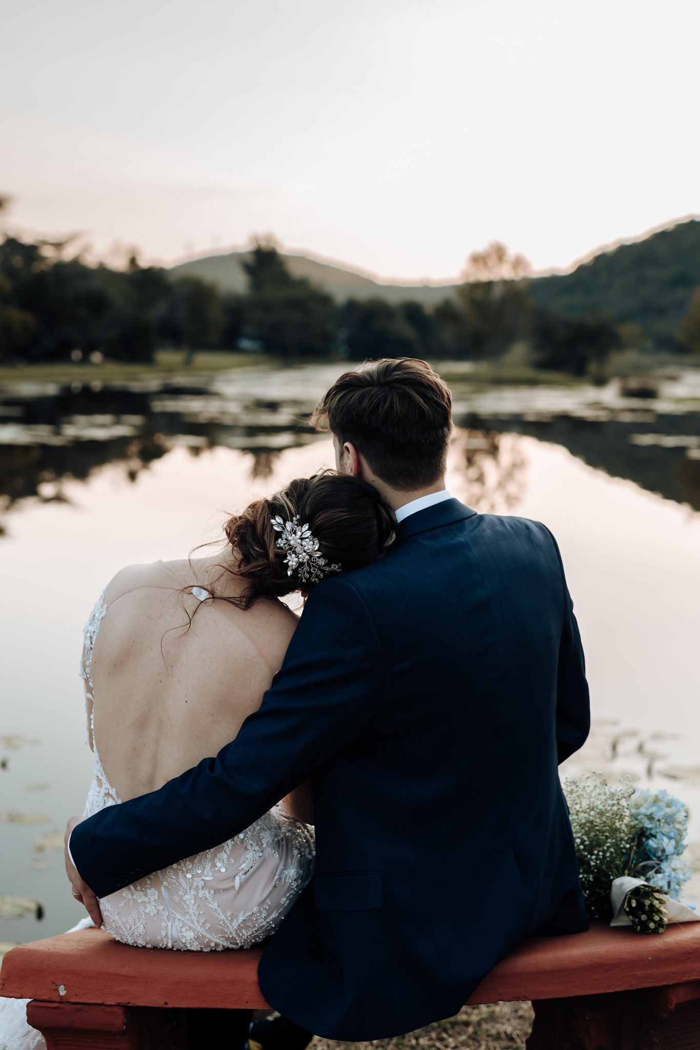 Sunset silhouette of couple sitting together on bench by peaceful lake with mountain reflections.