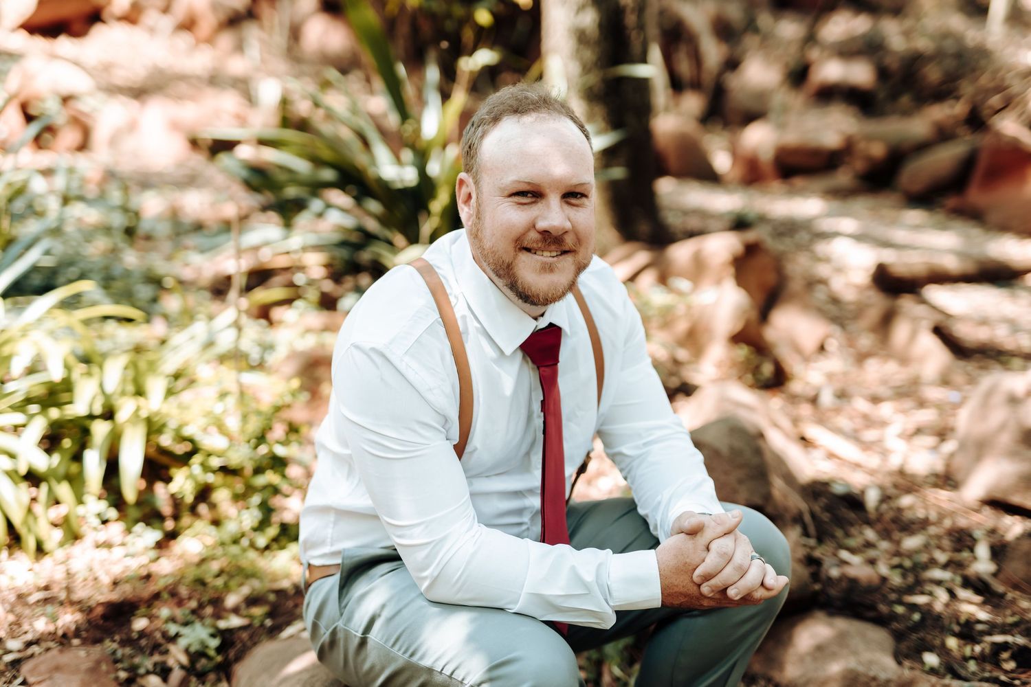 Person in white dress shirt and red tie sitting outdoors in a garden setting.