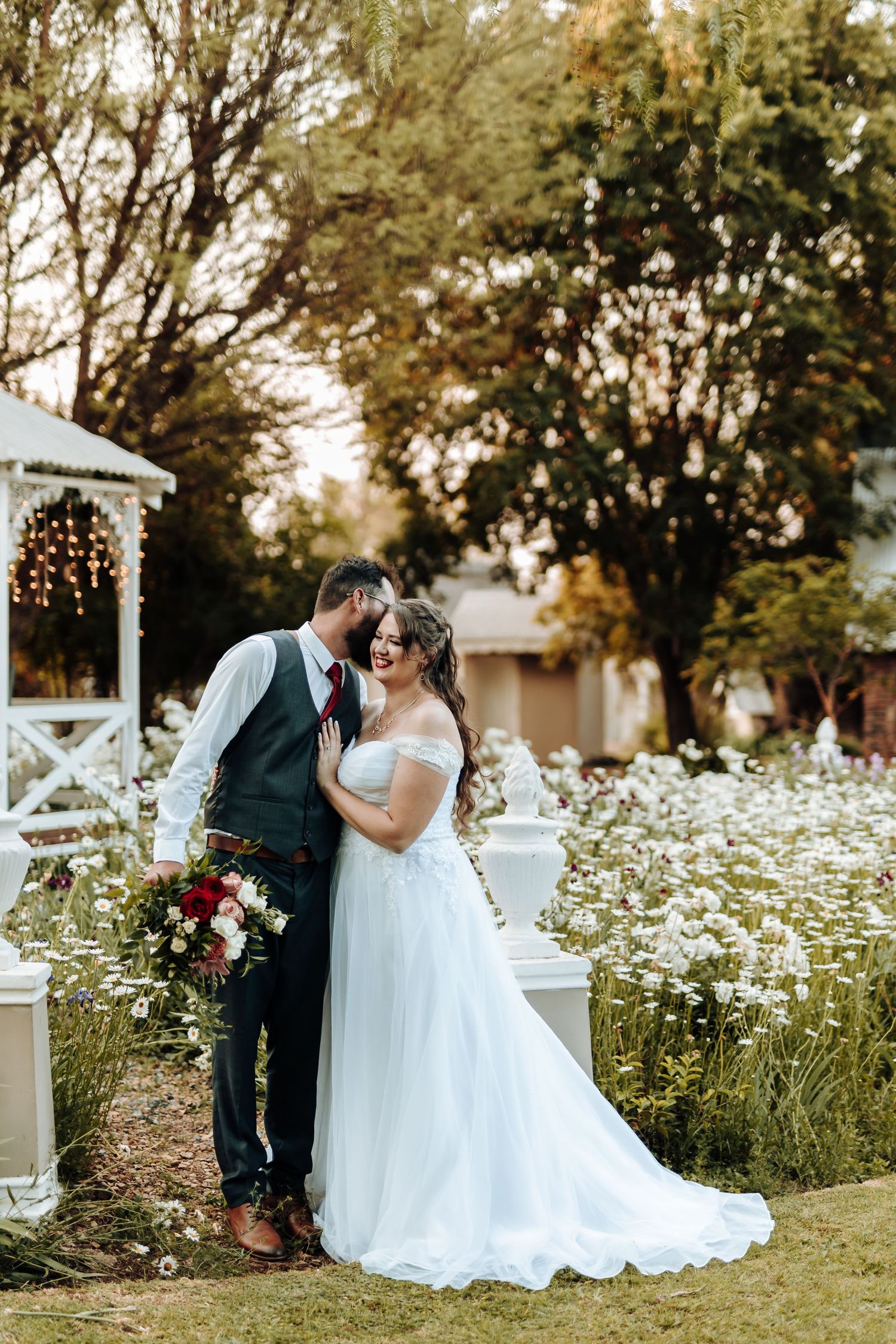 Intimate moment between newlyweds by decorated gazebo in wildflower garden at dusk.