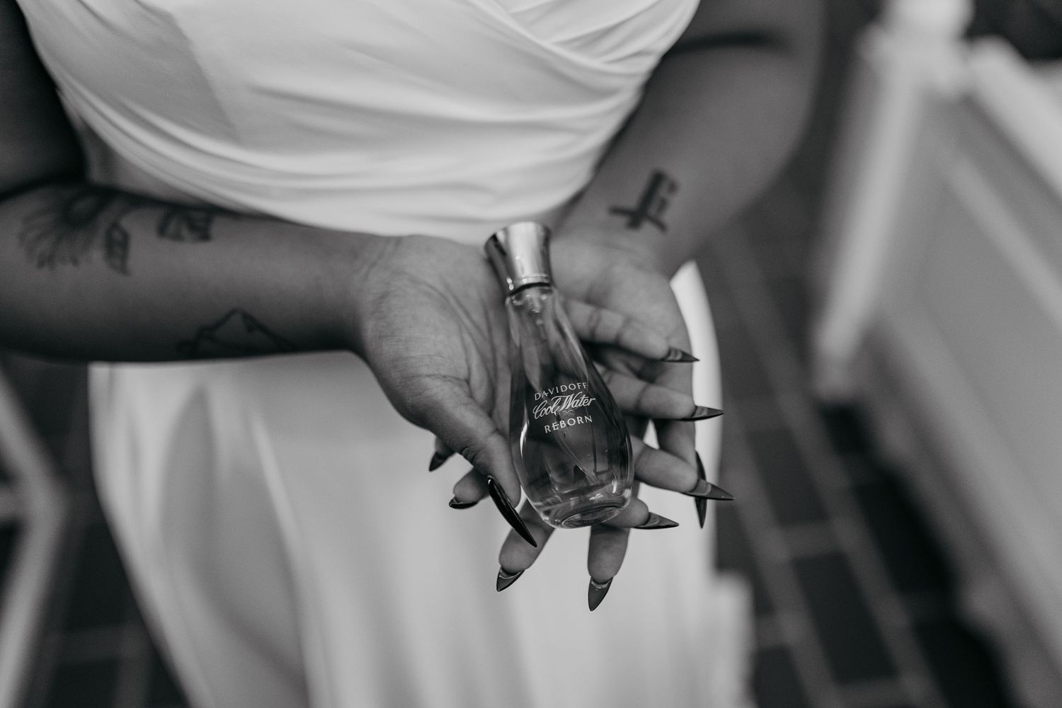Black and white image showing hands holding a glass perfume bottle in an elegant pose.