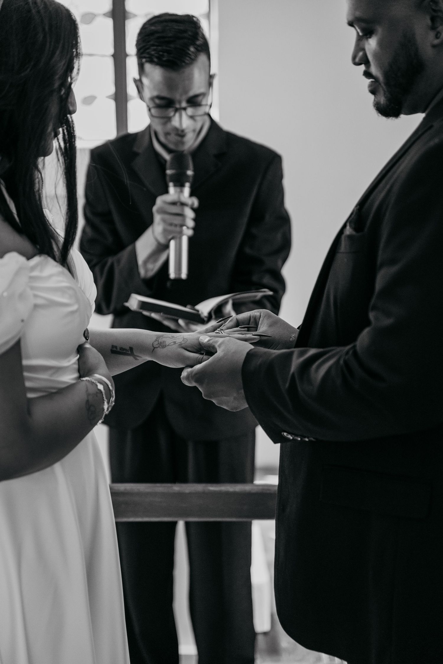 Wedding ceremony with couple exchanging rings as officiant holds microphone in black and white photo.