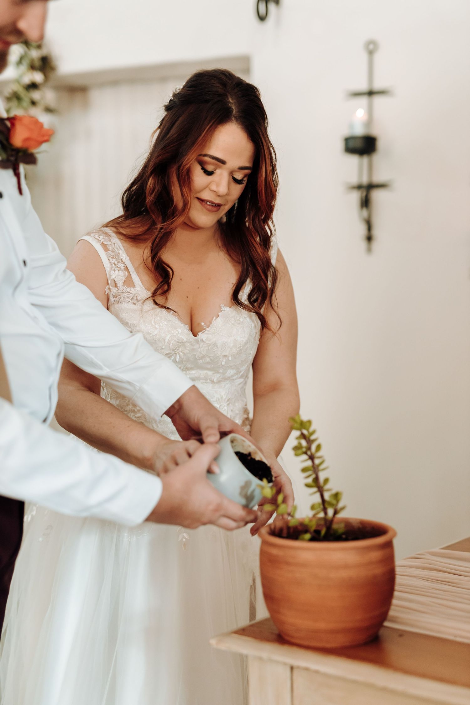 Close up of a white lace wedding dress being adjusted near a potted plant.