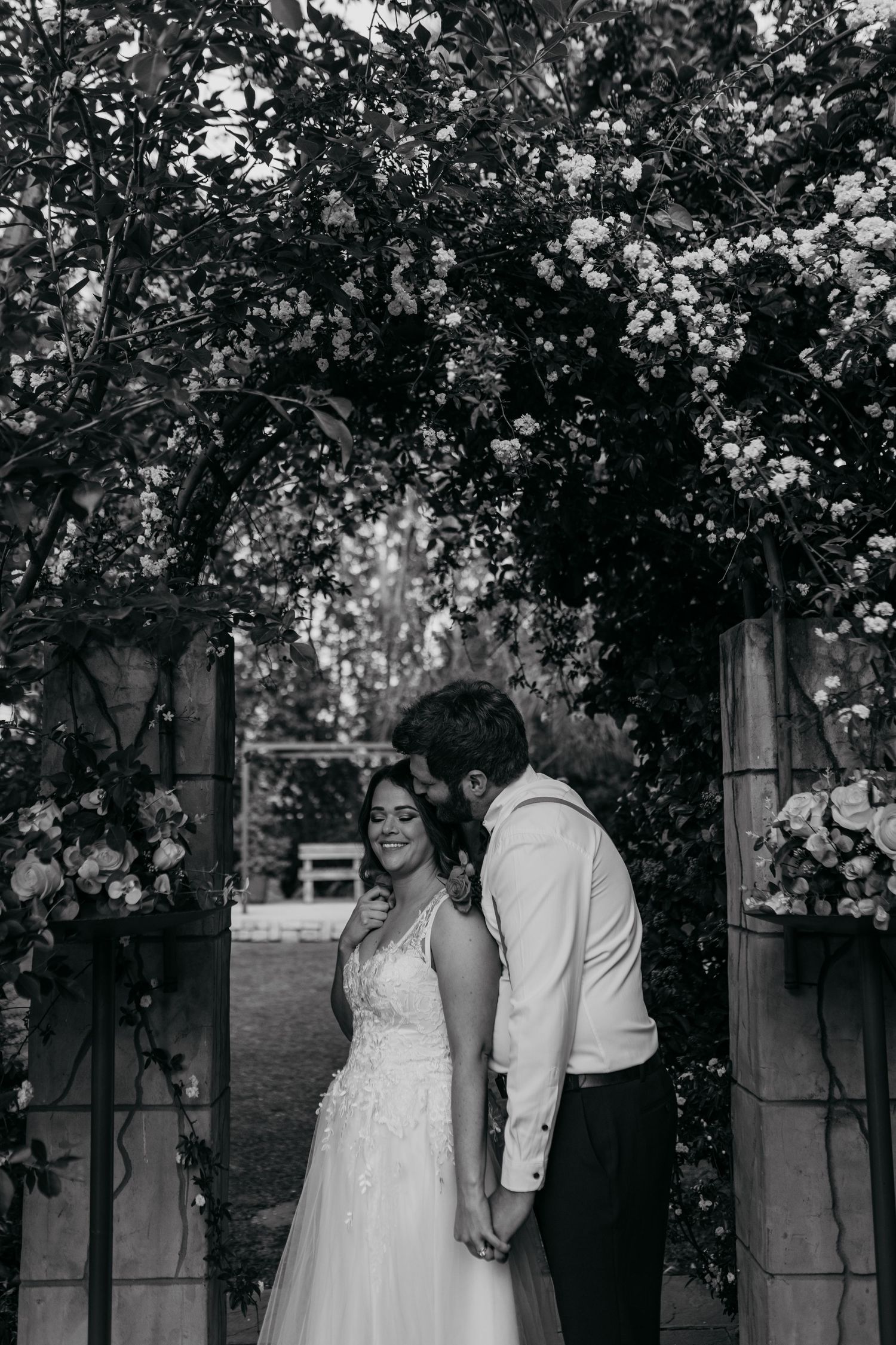 Black and white portrait of couple sharing intimate moment under floral arch.