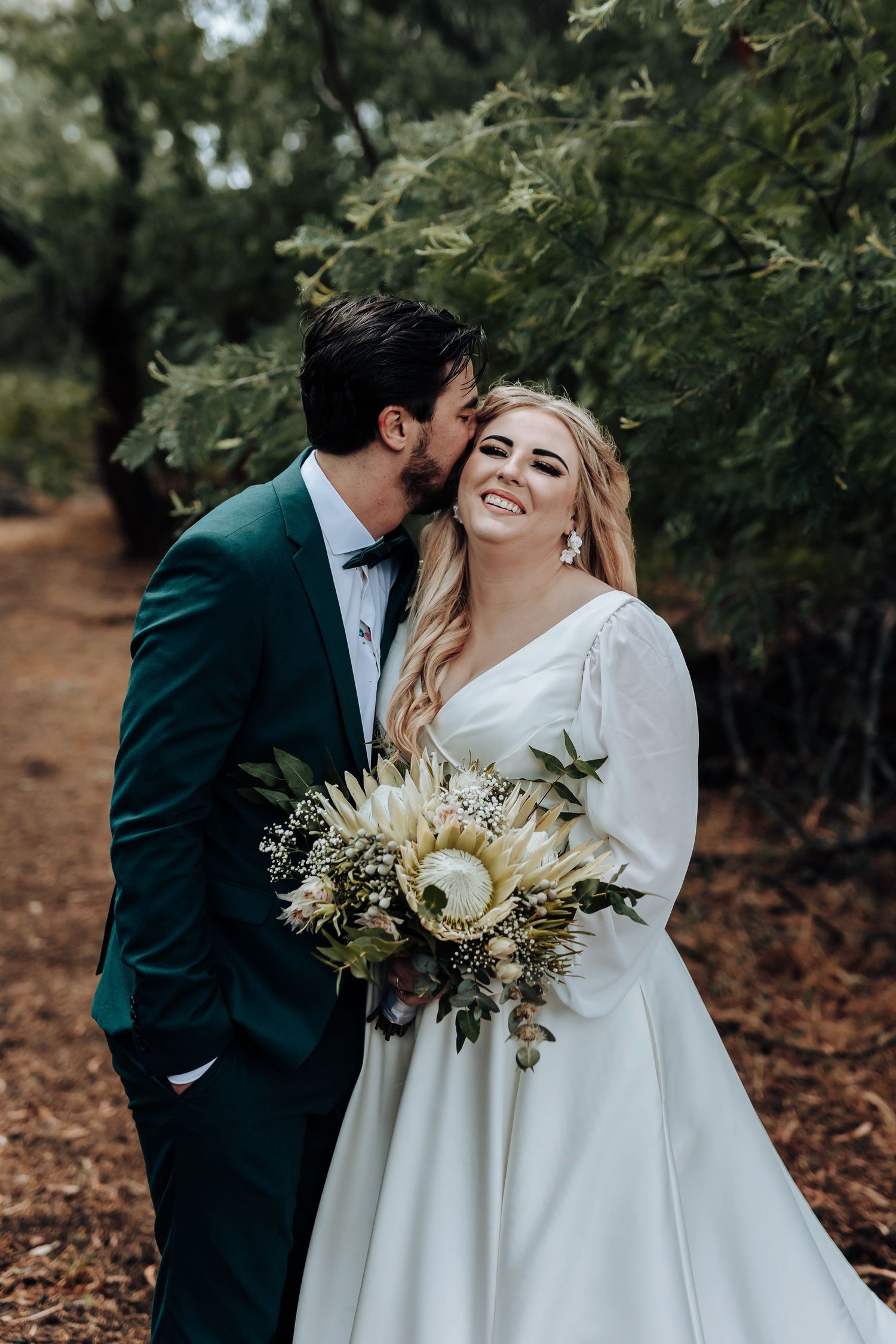 Joyful wedding moment captured in forest with couple laughing and neutral toned bouquet.