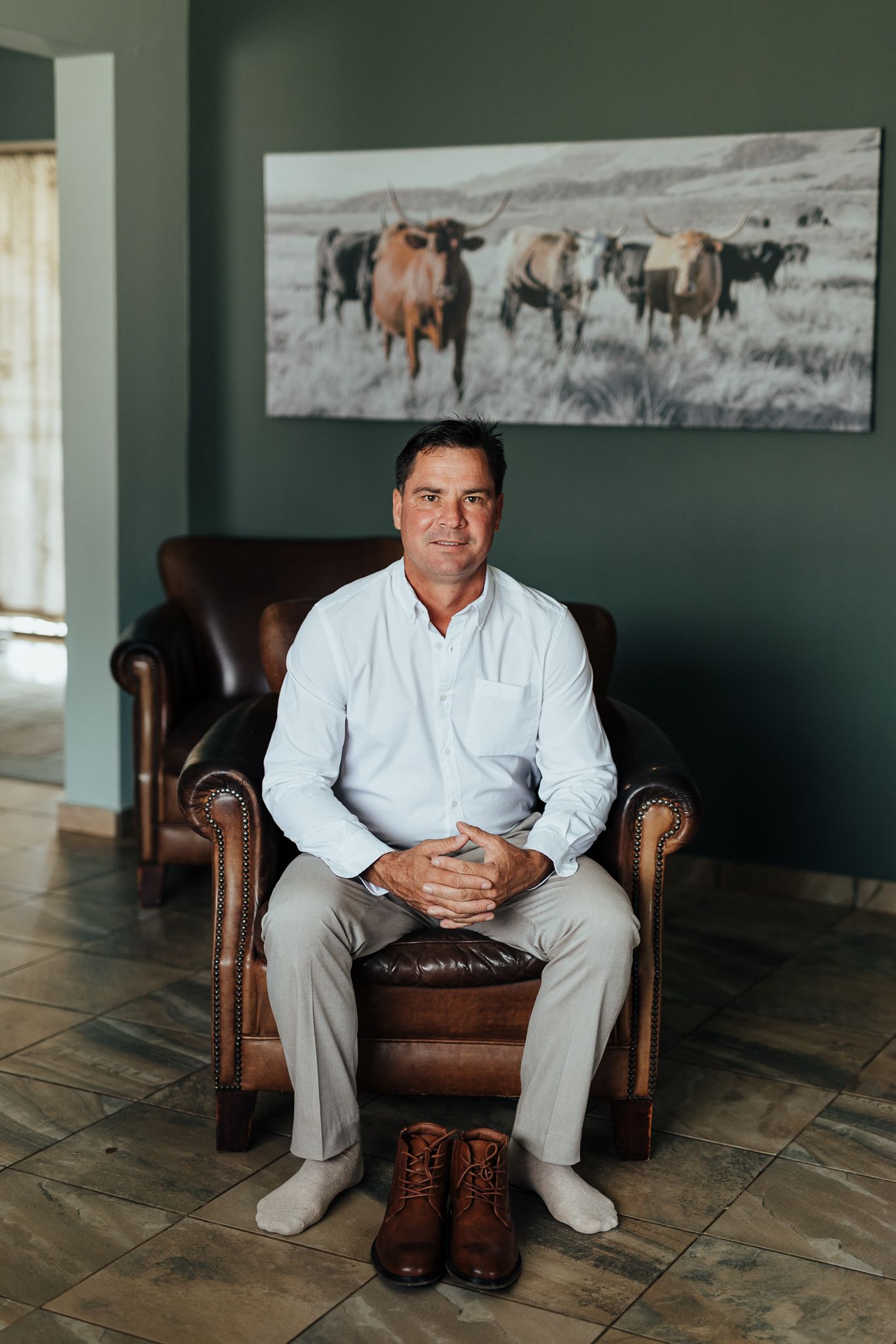 Portrait in leather armchair with brown boots and horse artwork displaying formal attire.