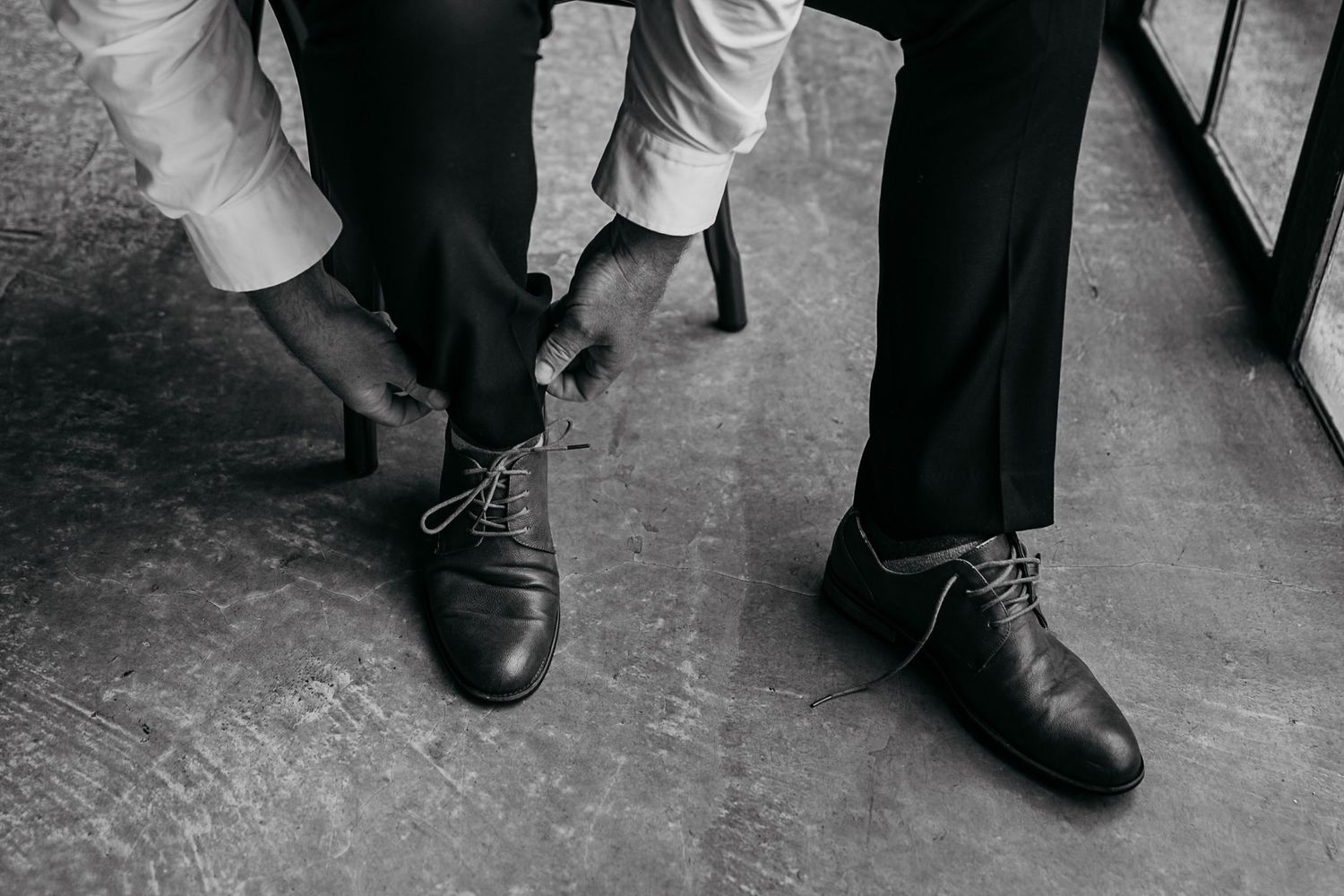 Close-up view of black leather dress shoes and pant legs on a concrete floor.