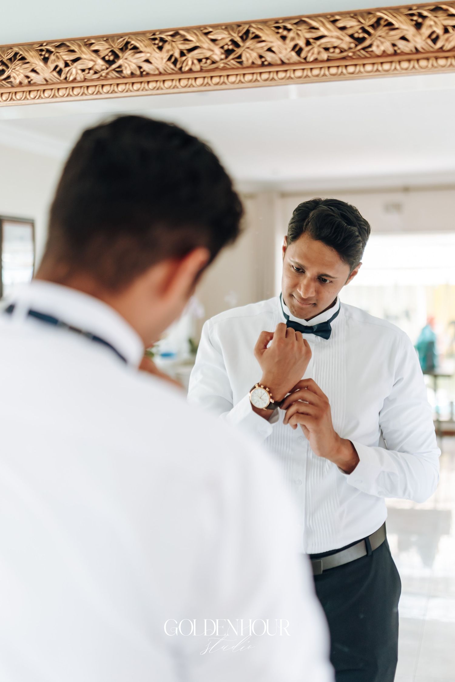 Groom in white shirt and black pants wipes tears away during emotional wedding day preparation.
