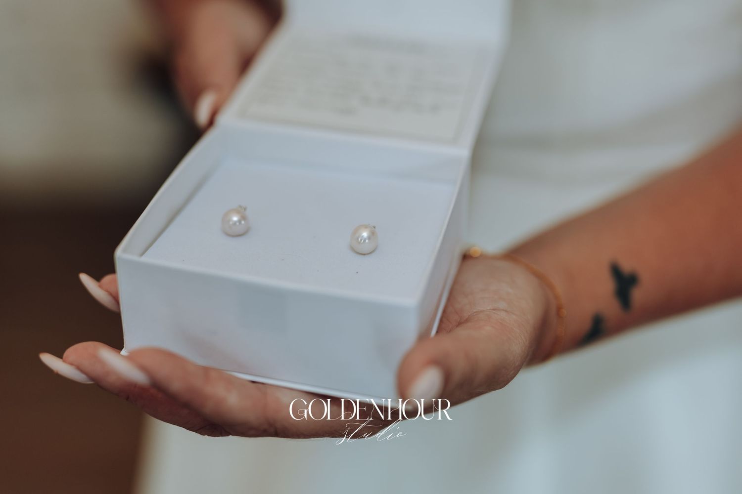 Close-up view of hands opening a small white jewelry box containing pearl earrings.