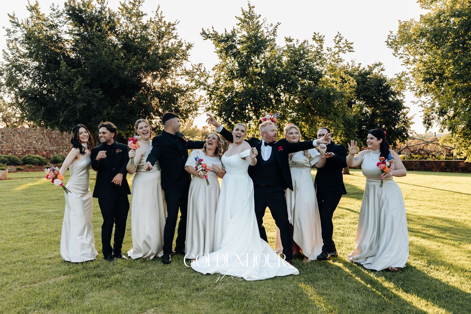 Wedding party relaxes on a grassy hill during golden hour at an outdoor celebration.