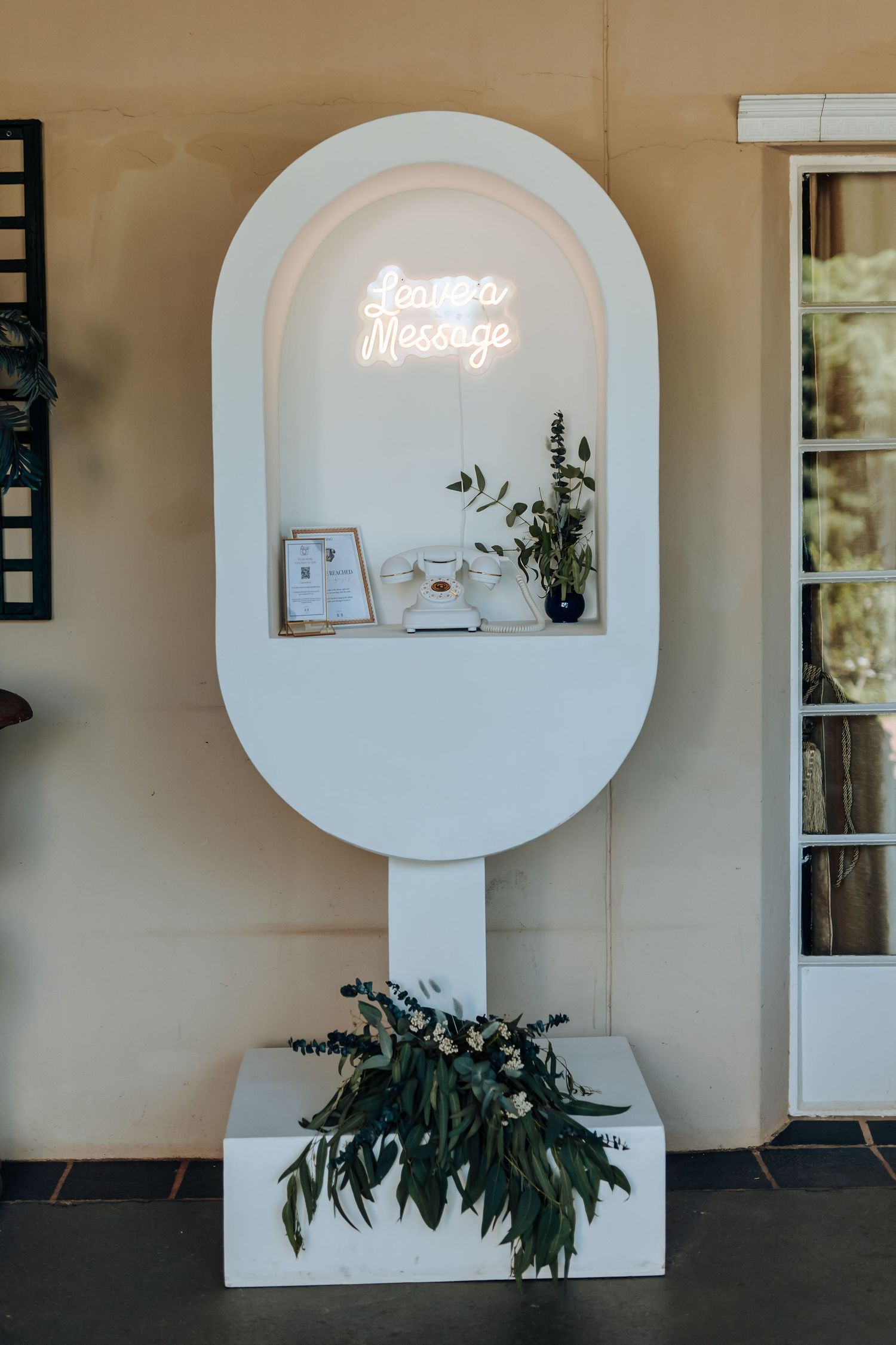 Modern white oval-shaped display stand with neon message sign and decorative plants in an elegant interior setting.