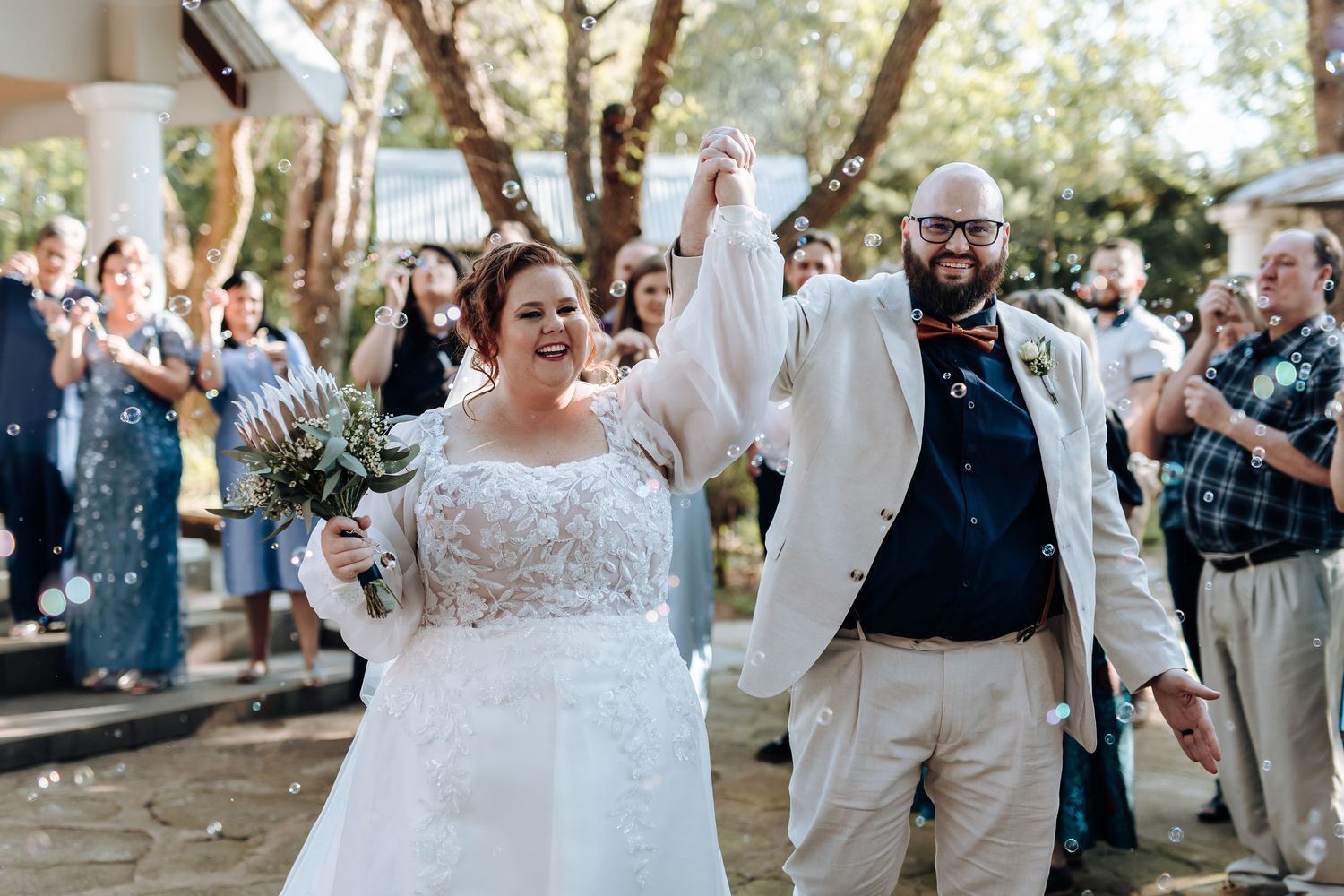 Wedding guests celebrate and dance together during an outdoor reception in a garden setting.