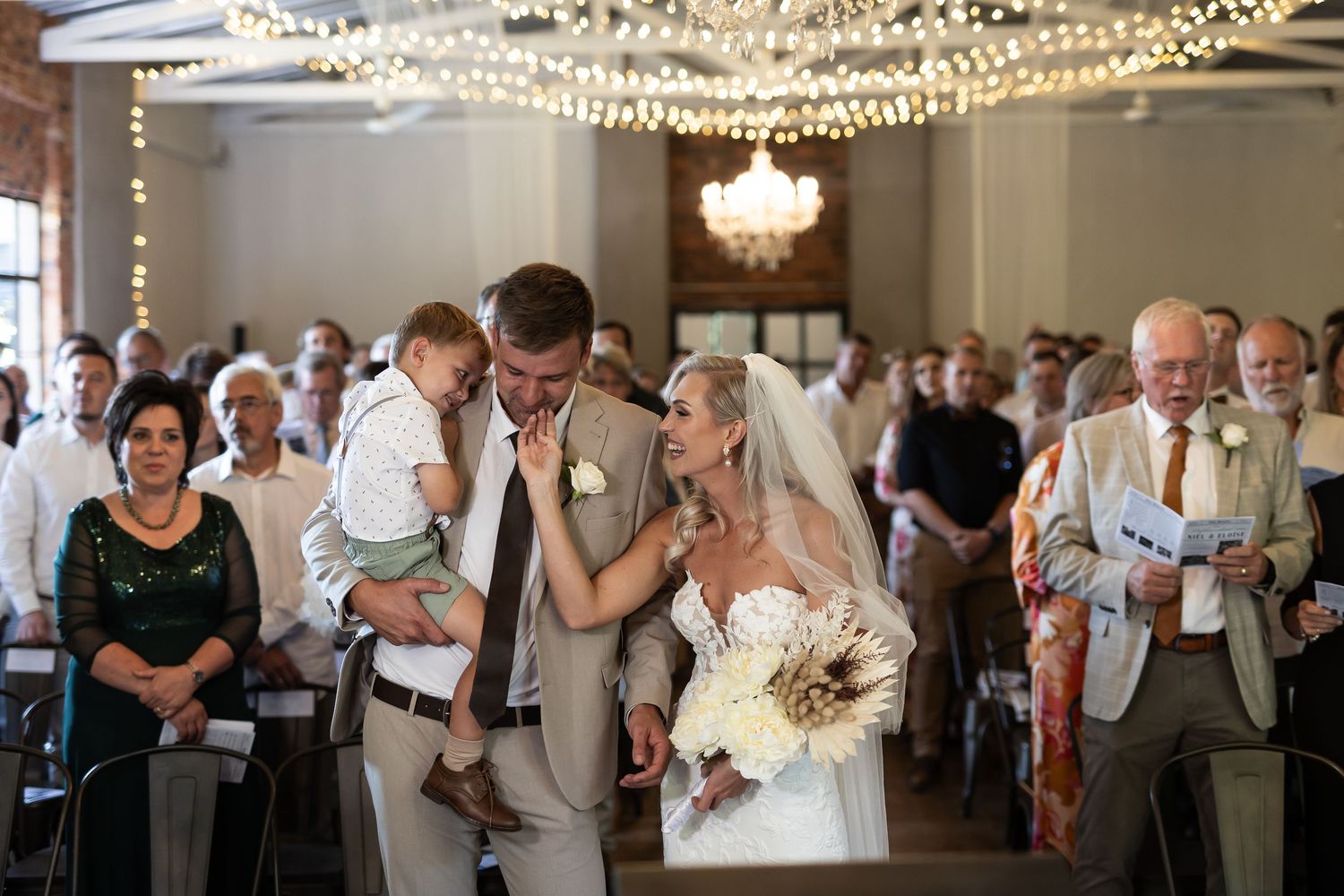Guests dance and celebrate on a wedding reception dance floor beneath elegant string lights and chandeliers.