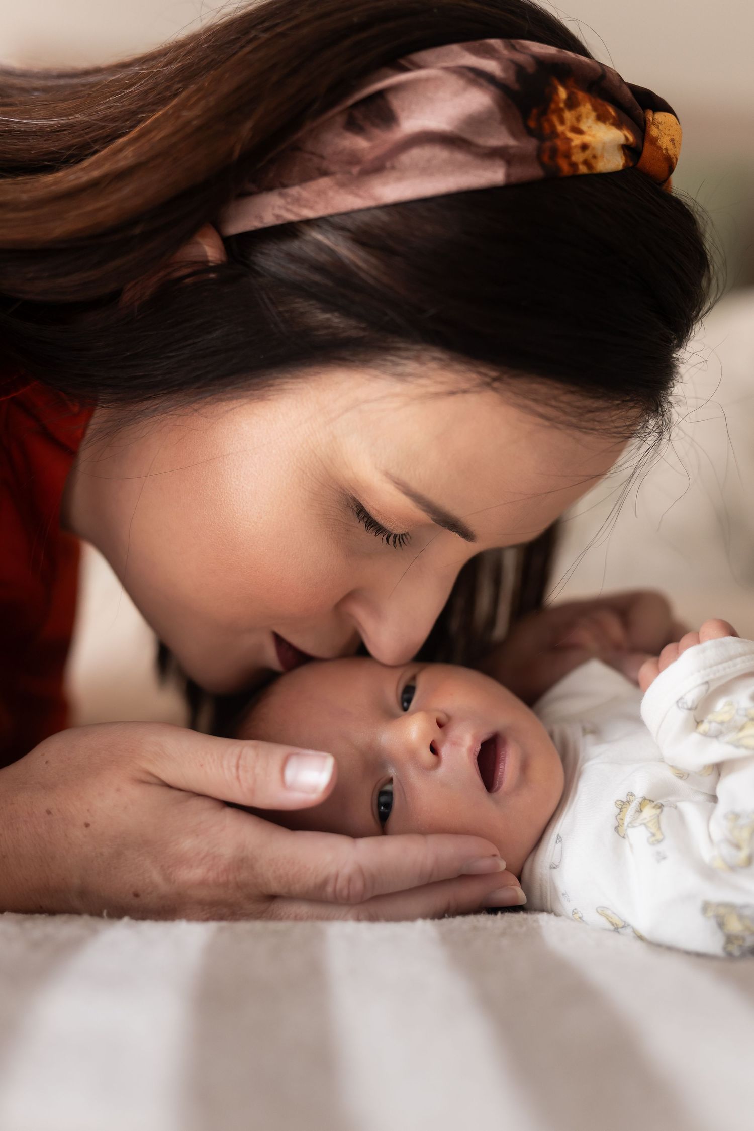 A tender moment between parent and newborn captured in an intimate photo series on white bedding.