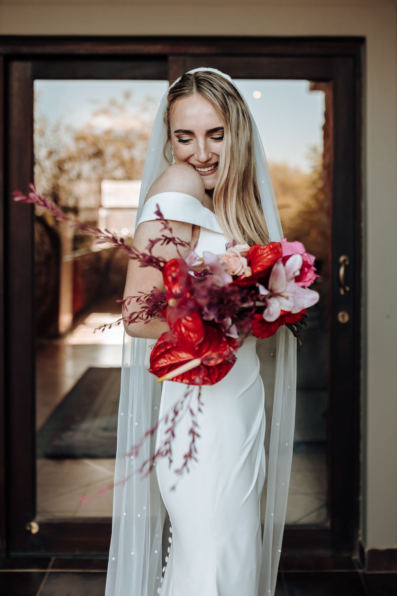 Joyful bridal portrait with cascading red flowers and off-shoulder wedding dress.