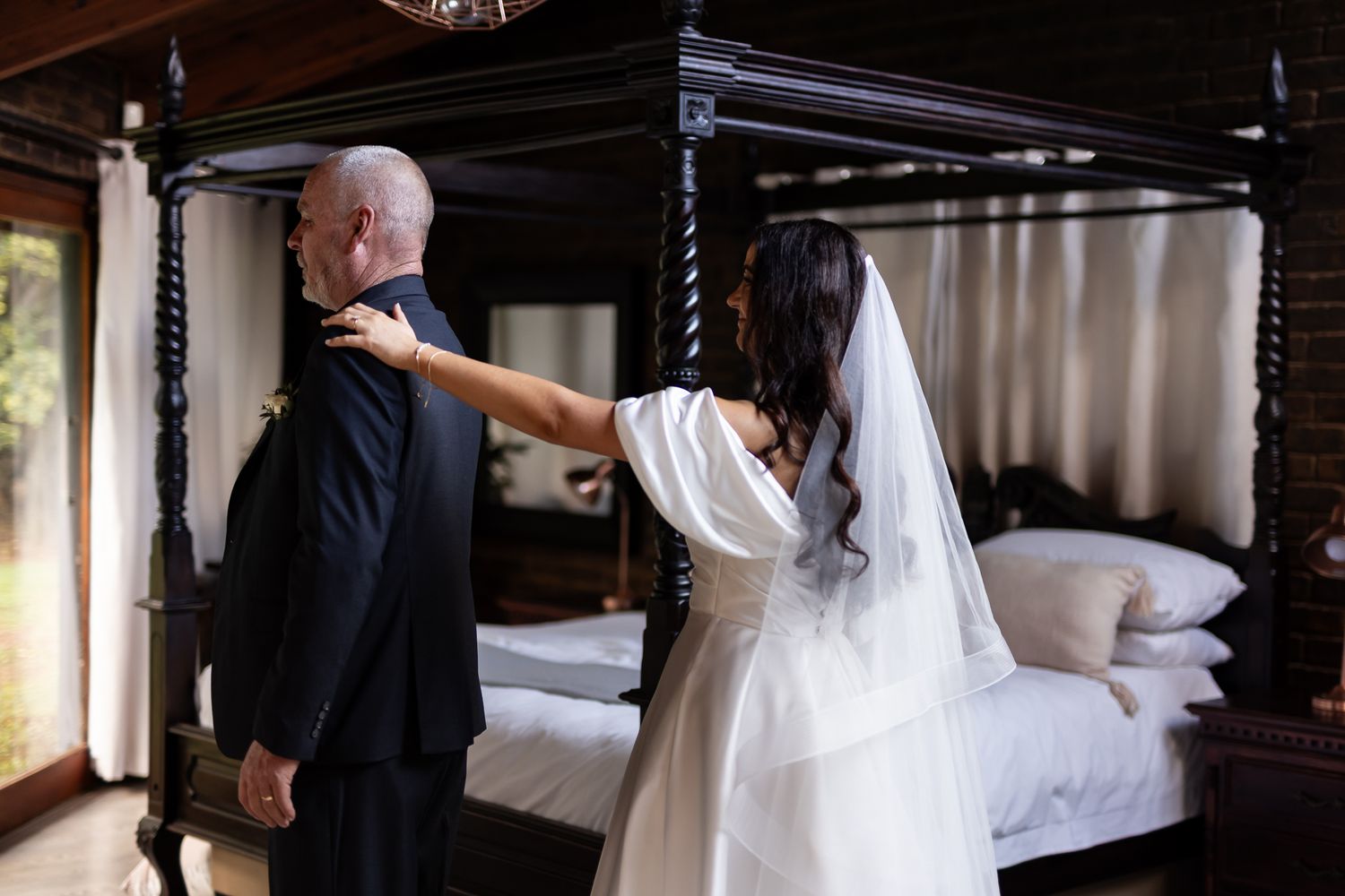 A touching moment between two people in a bedroom, with one wearing a bridal gown and veil.