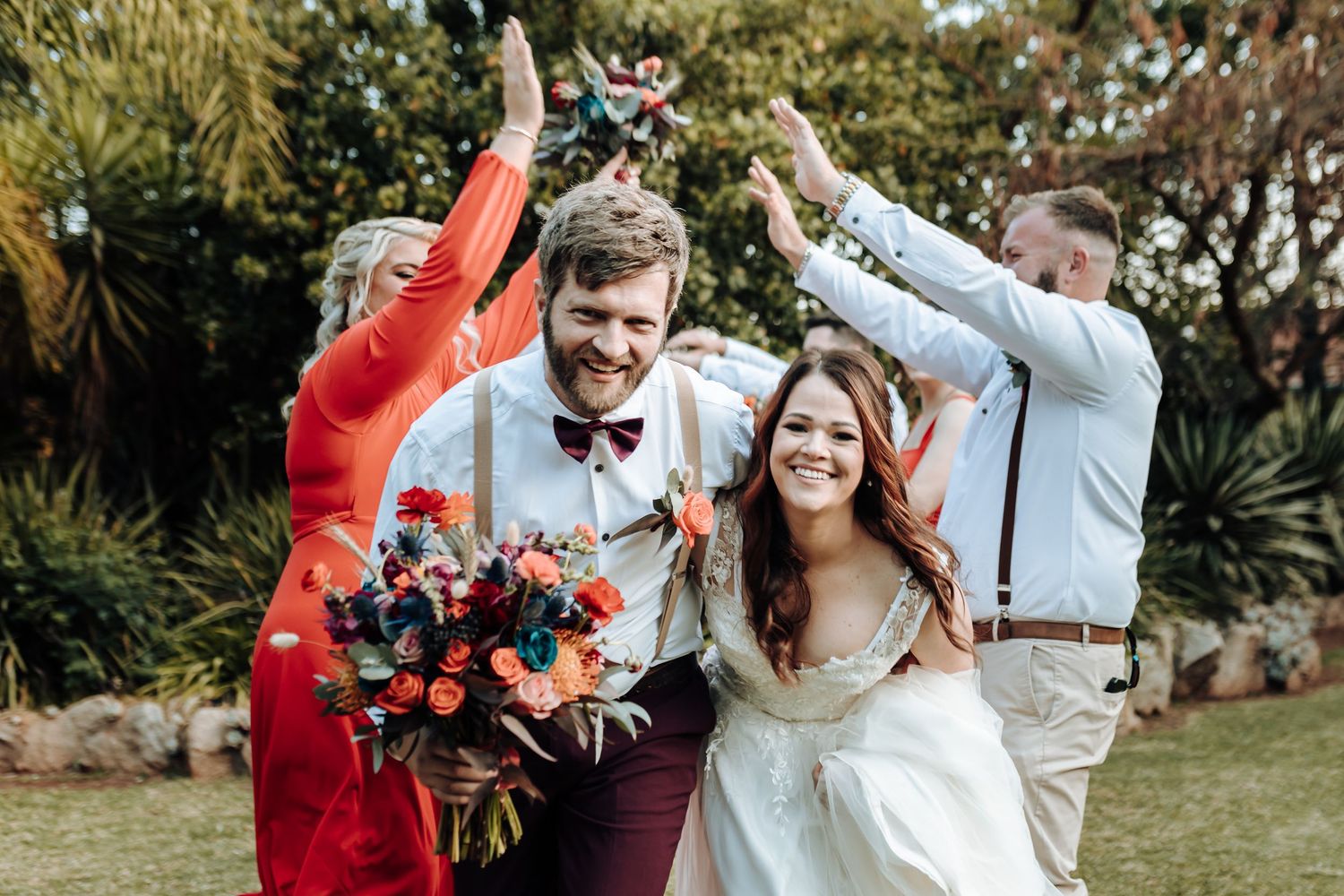 Candid celebration moment of wedding party jumping and cheering outdoors.