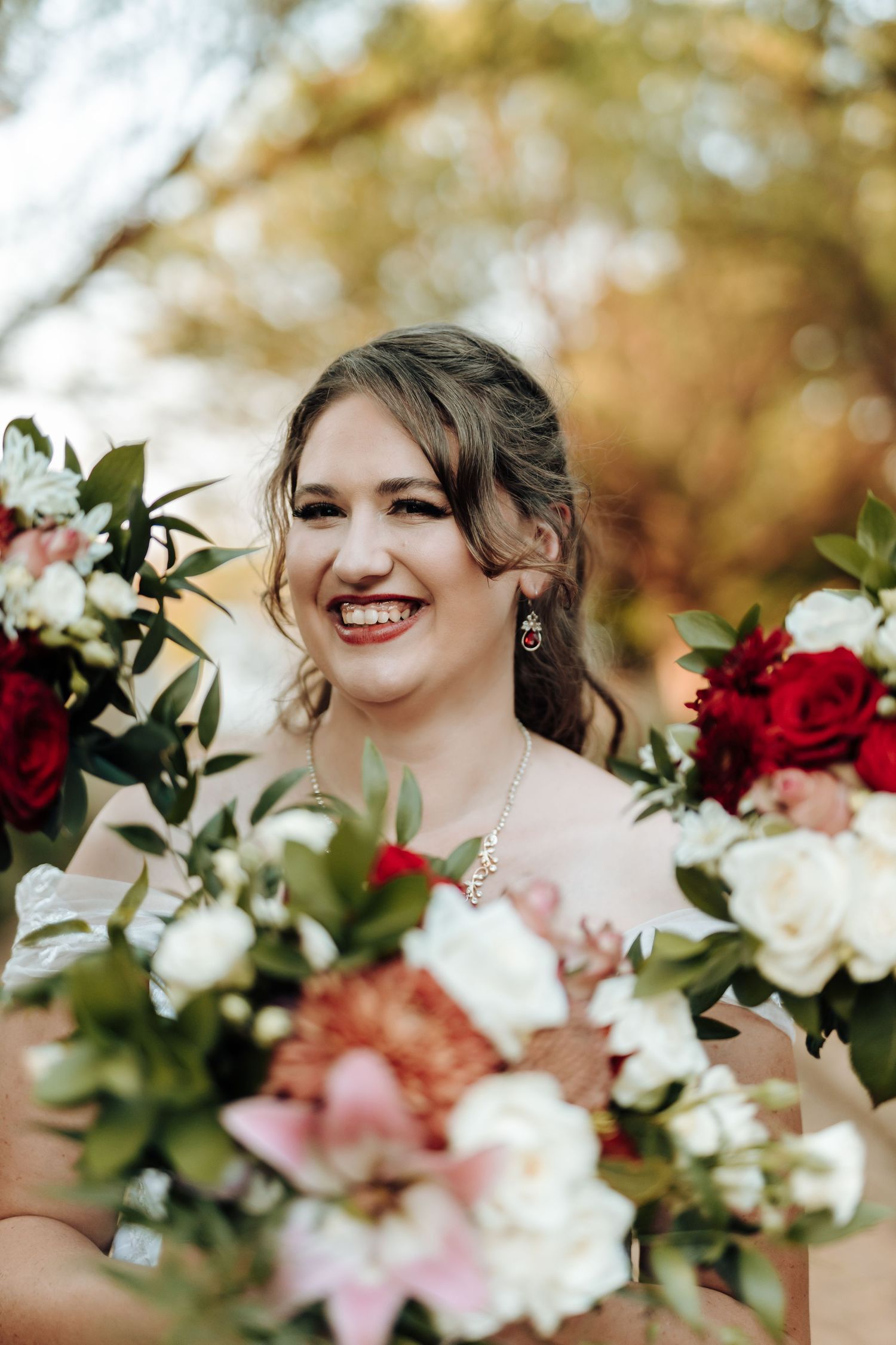 Close-up portrait with vibrant wedding bouquet featuring red roses and white flowers.