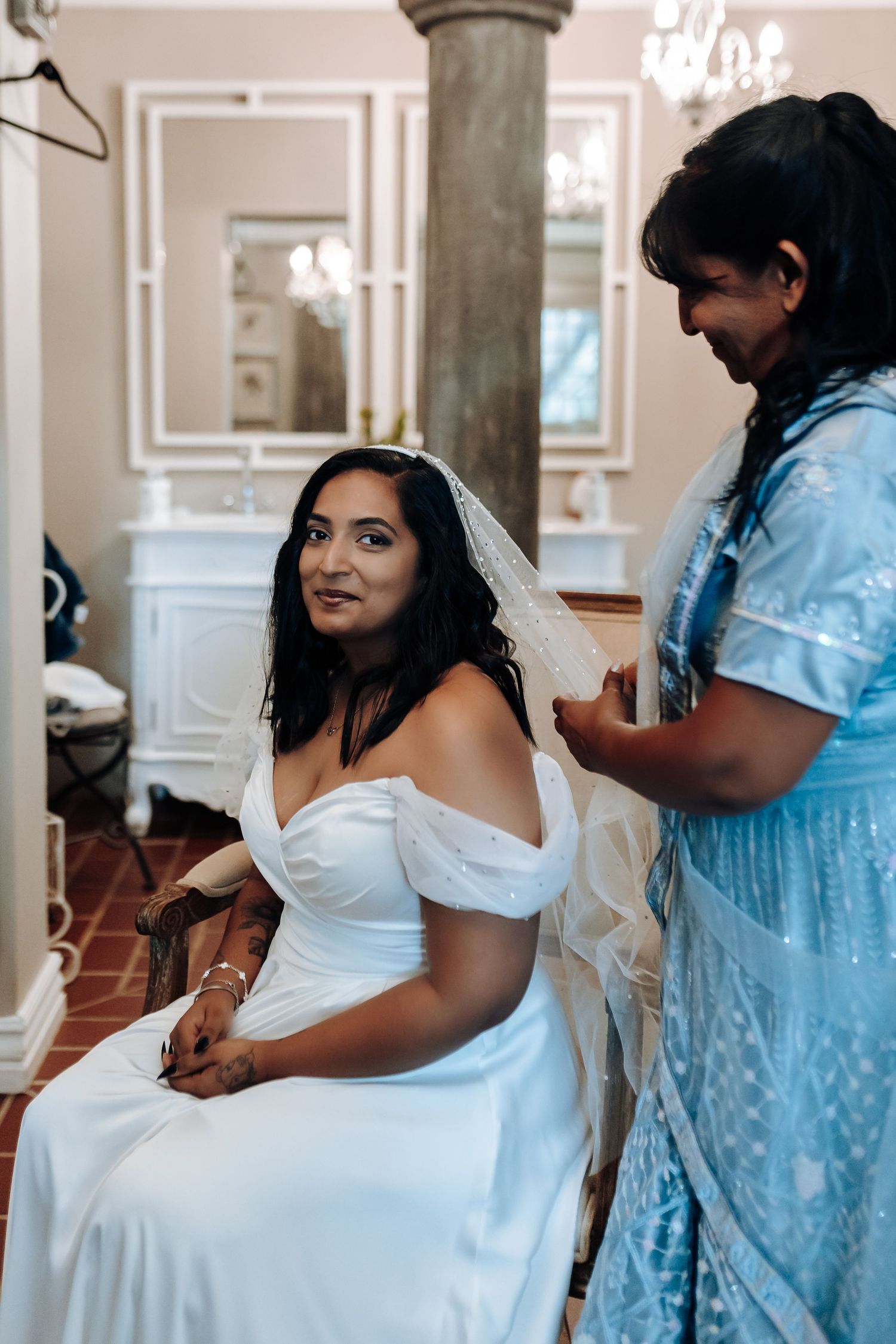 Getting ready moment as bride in white dress receives final preparations in elegant room.