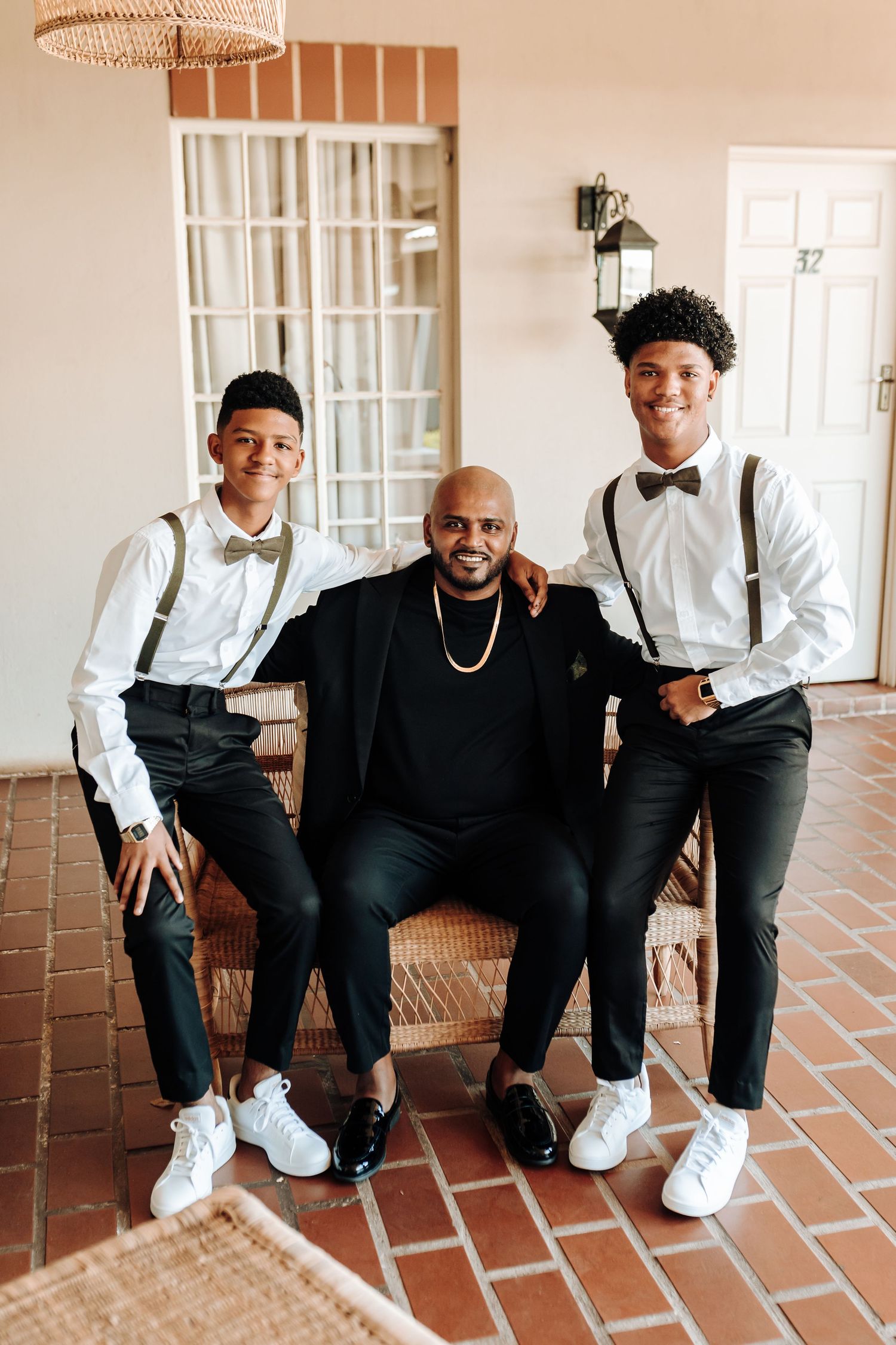 Three people in formal attire posing together on brick flooring with rattan decor.