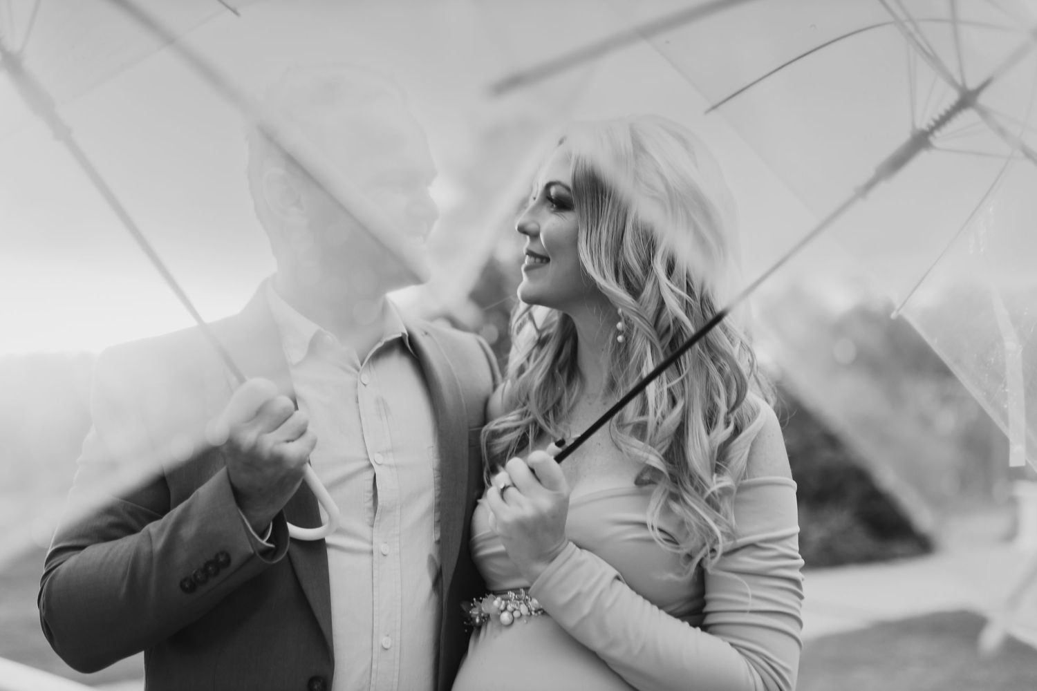 A romantic black and white portrait of a couple embracing outdoors in winter coats during a snow-filled day.