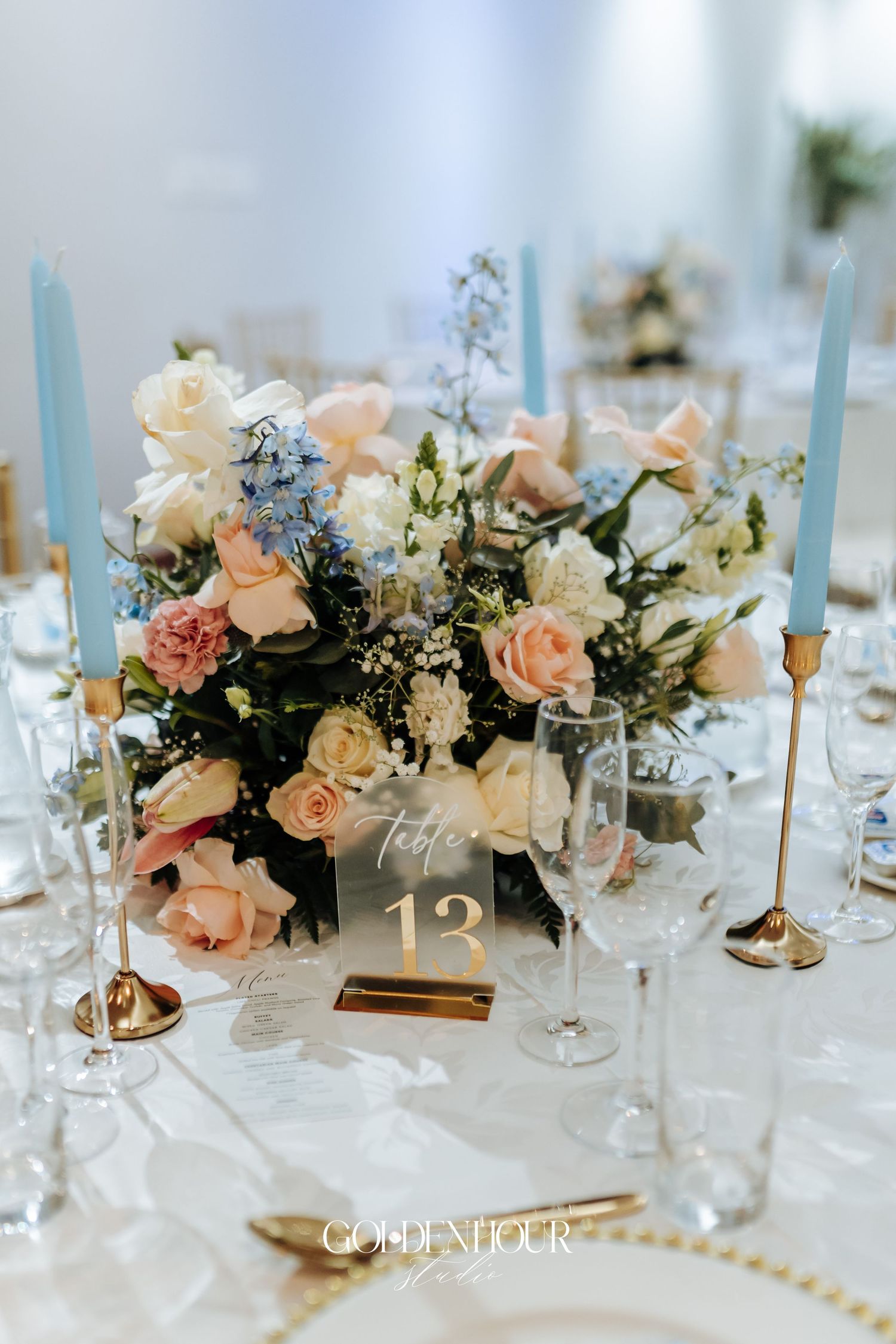 Elegant table setting with peach roses, blue candles, and crystal glassware for wedding reception.
