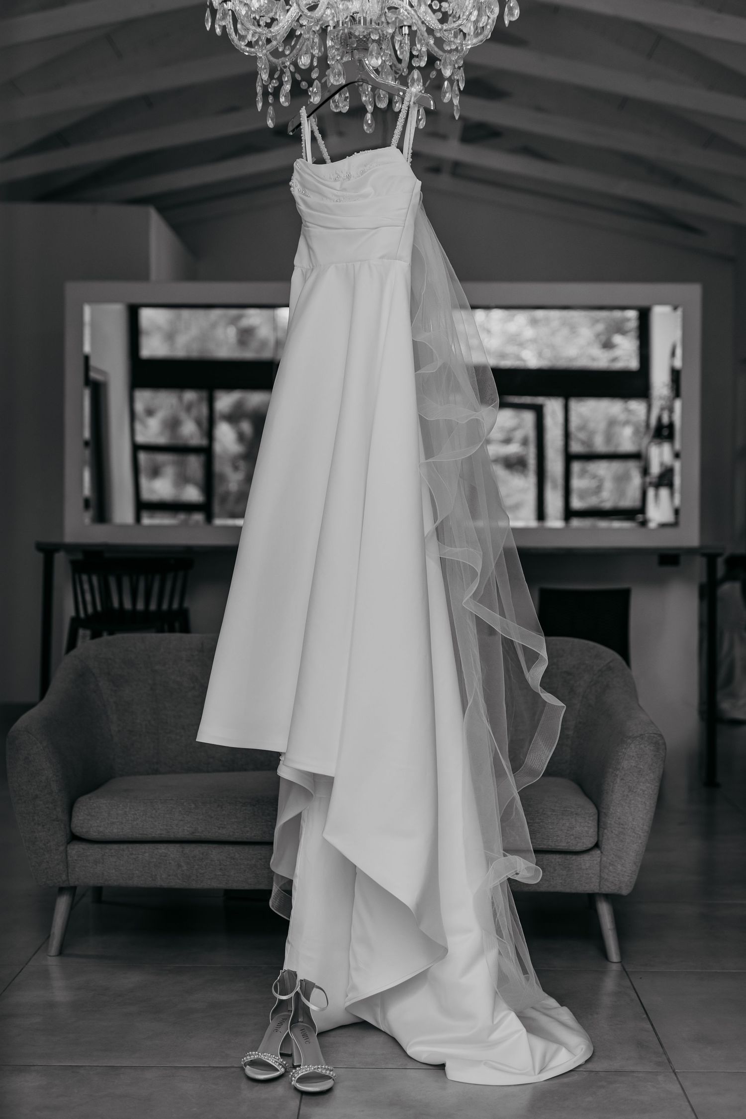 White wedding dress with flowing train displayed under an elegant crystal chandelier in a modern interior.