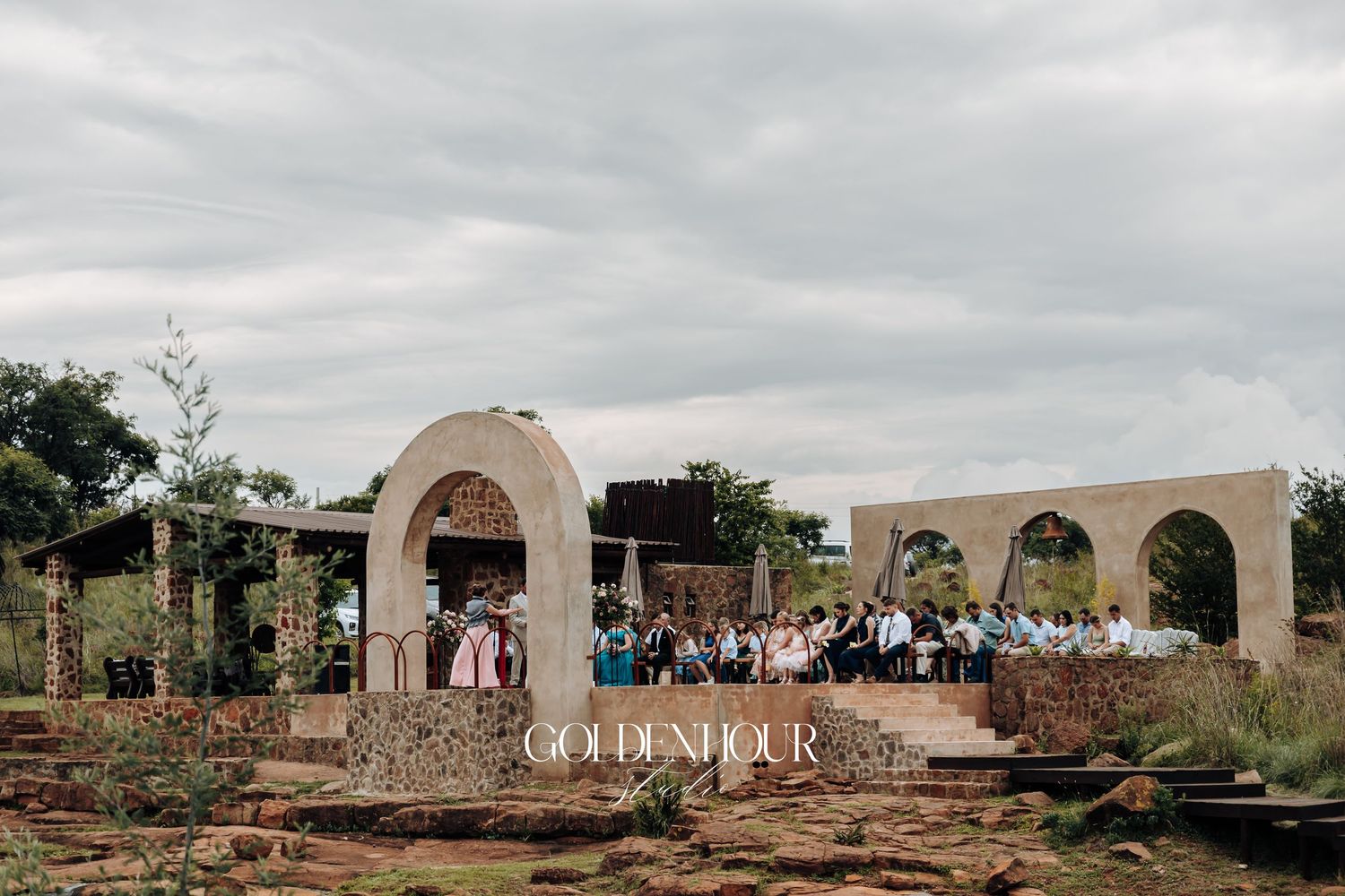 Wide view of outdoor wedding venue with stone archways and gathered guests.