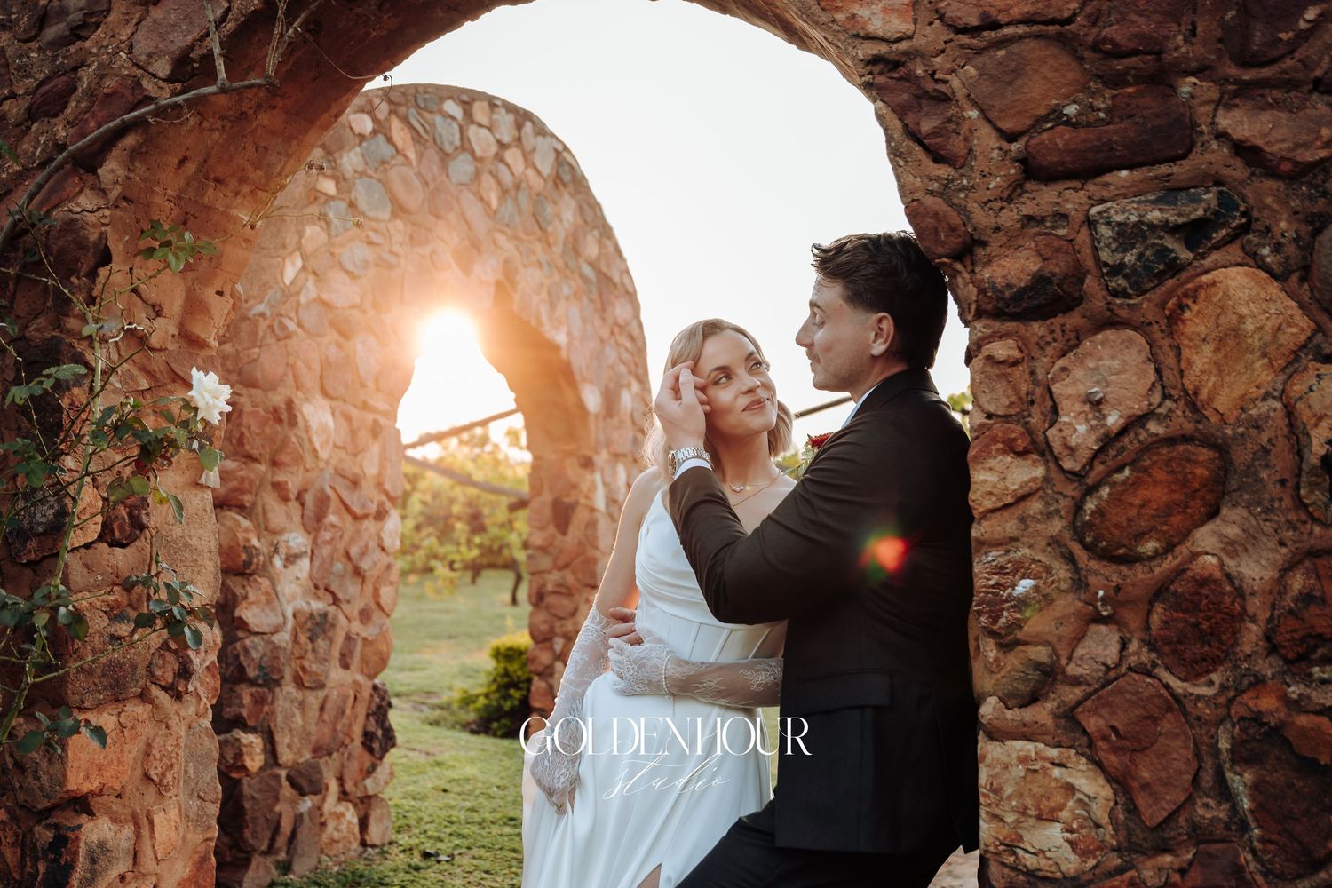 Newlyweds sharing intimate moment under stone archway at sunset.