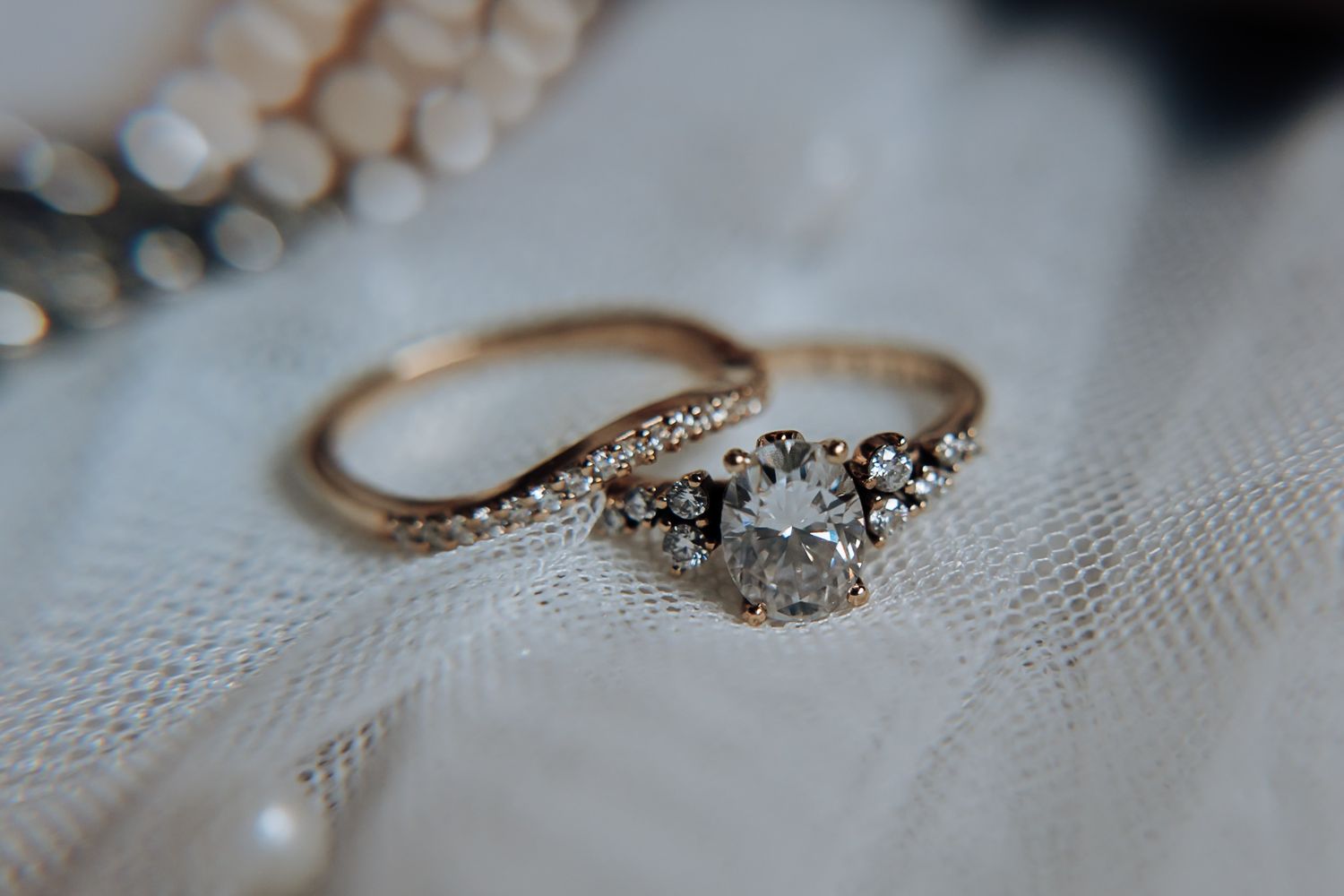 Close-up view of elegant engagement rings with diamonds and pearls on white lace fabric.