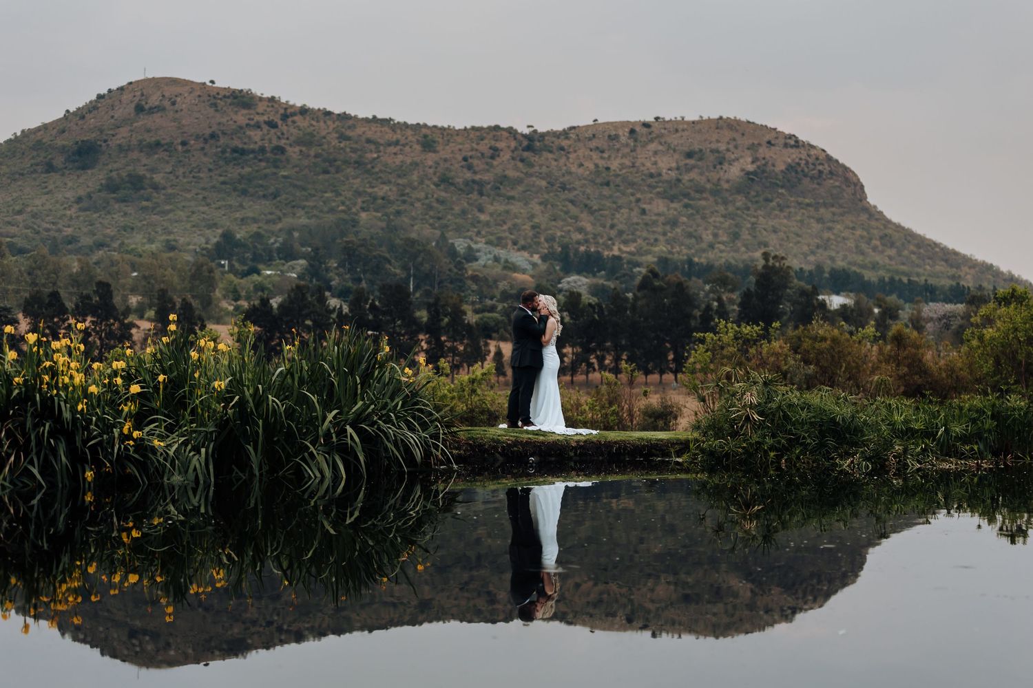 A scenic mountain landscape with a serene lake reflecting the surrounding hills and wildflowers at sunset.