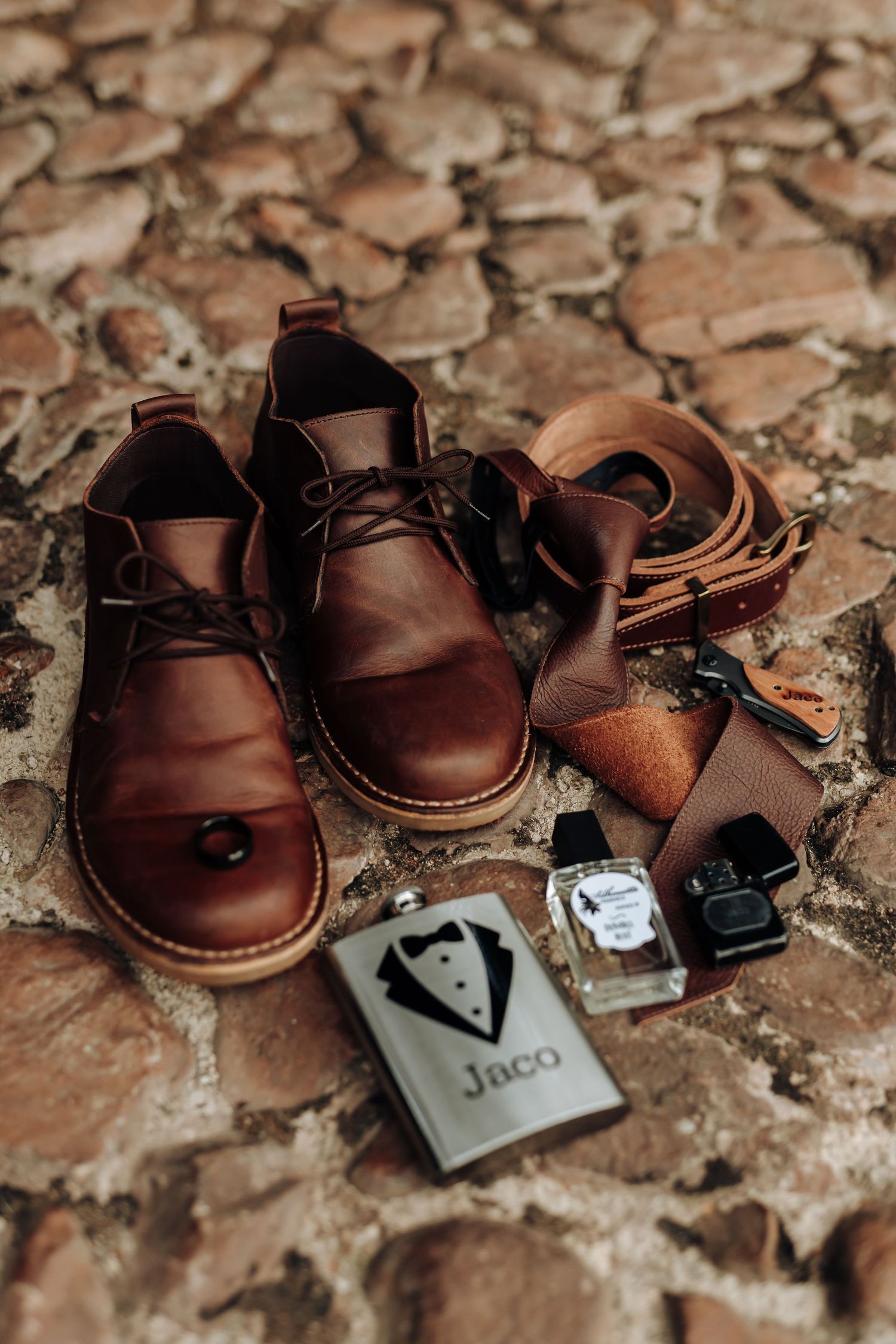 Brown leather baby shoes with bow tie accessory on rustic stone surface create charming wedding detail shot.