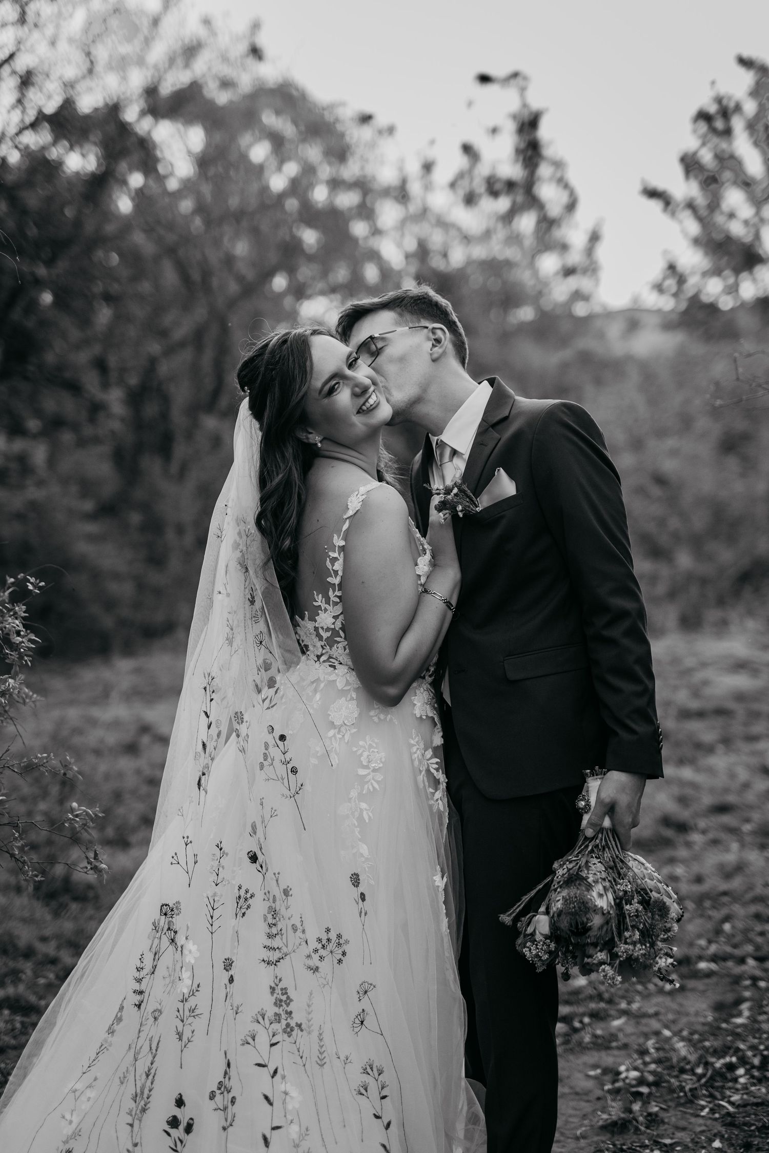 A romantic black and white wedding photo series showing a couple in an outdoor setting among trees.