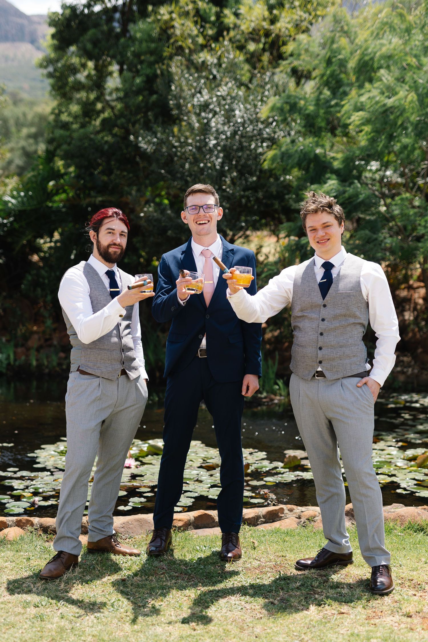 Groomsmen in formal attire pose playfully in a sequence of four candid photos by a pond with lily pads.