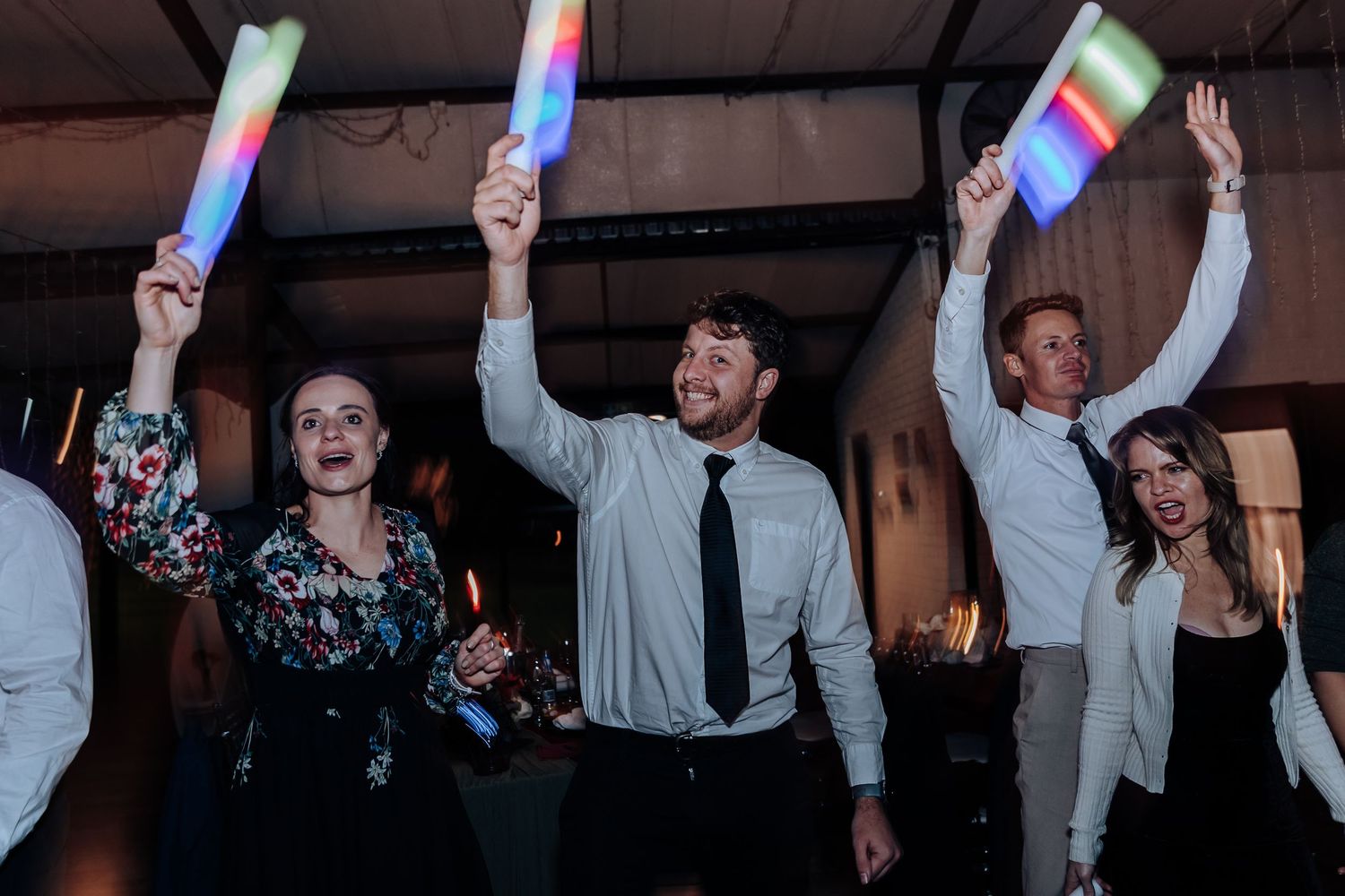 Guests dancing and raising colorful LED light sticks at a lively wedding reception celebration.