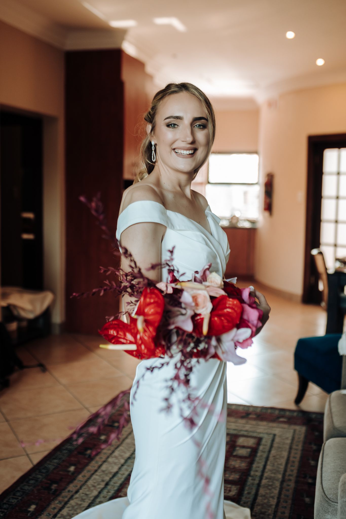 Elegant bridal pose with dramatic red floral bouquet in sunlit room.
