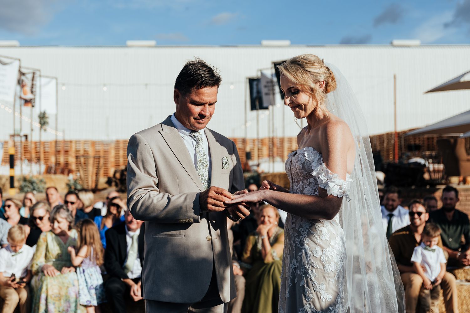 A wedding ceremony taking place outdoors with guests watching as couple exchanges vows.