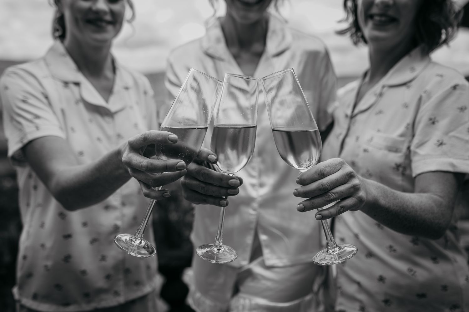 Black and white photo of hands toasting with champagne glasses on outdoor deck.