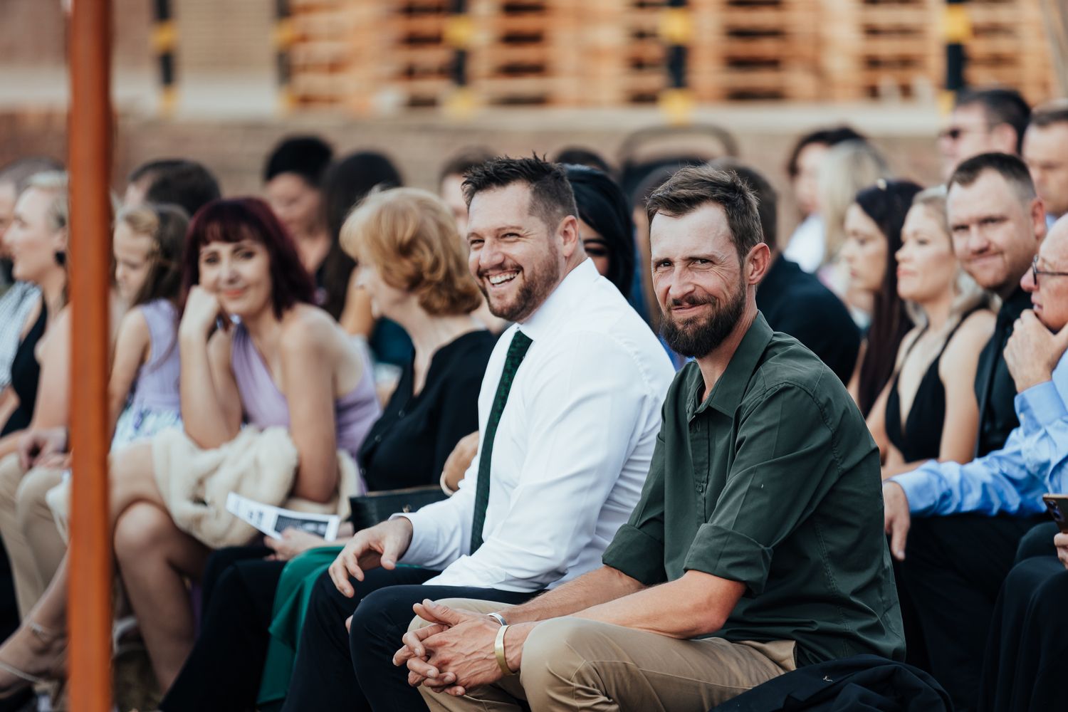 Wedding guests seated outdoors under covered venue watching ceremony.