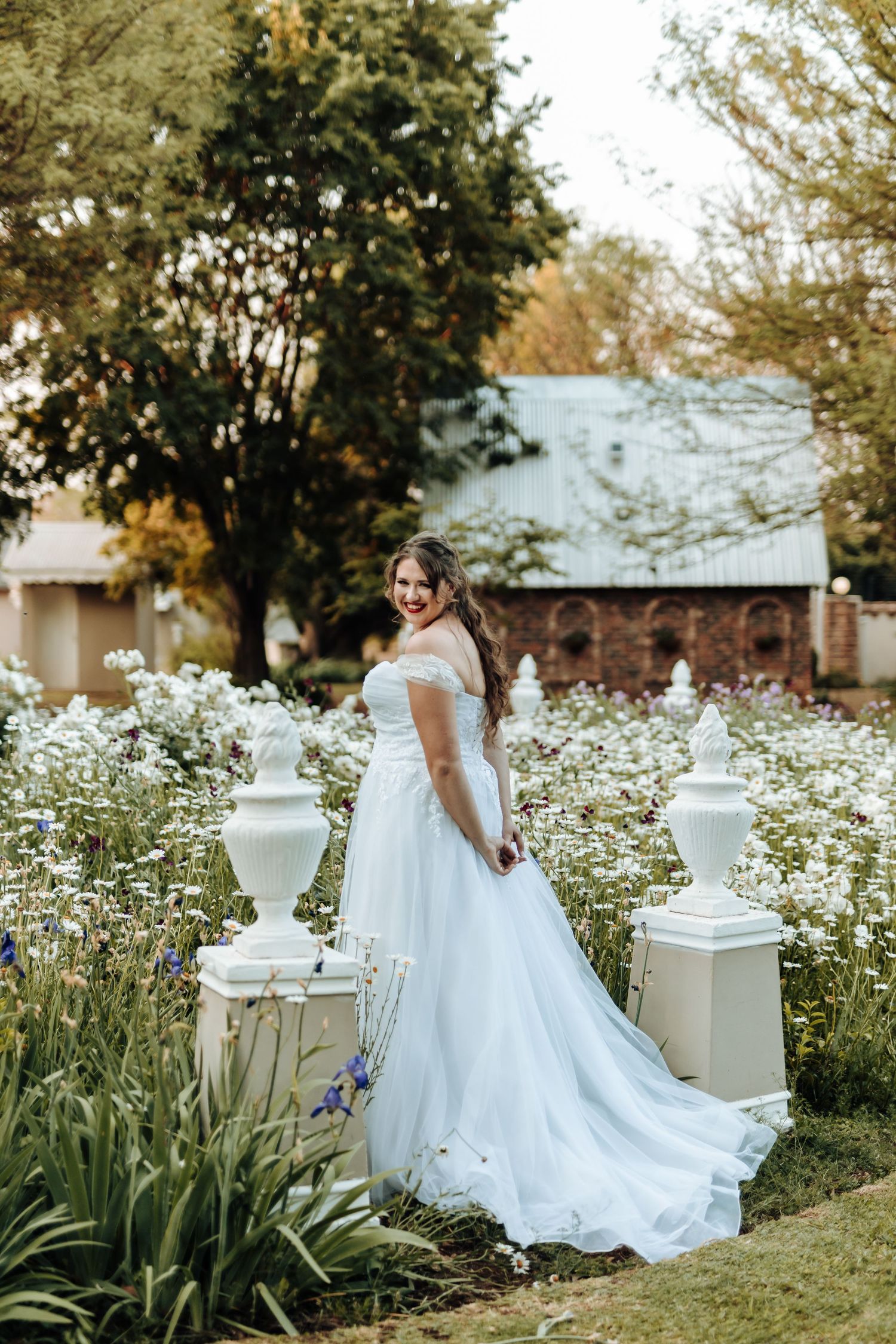 Elegant bridal photo showing detailed train of white dress among garden flowers and decorative posts.