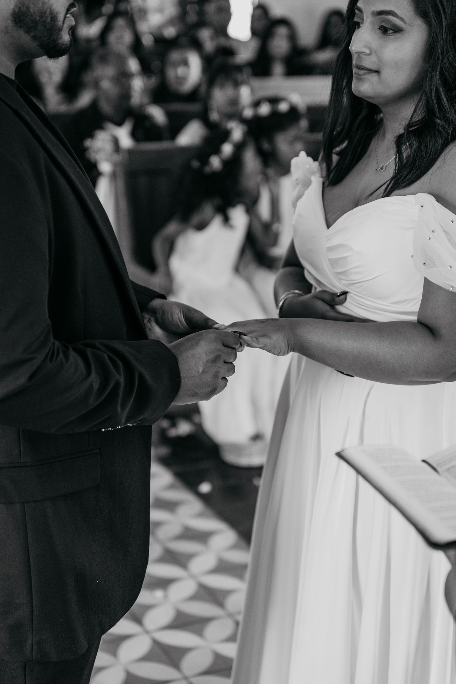 A black and white photo capturing an intimate moment during a wedding ceremony exchange.