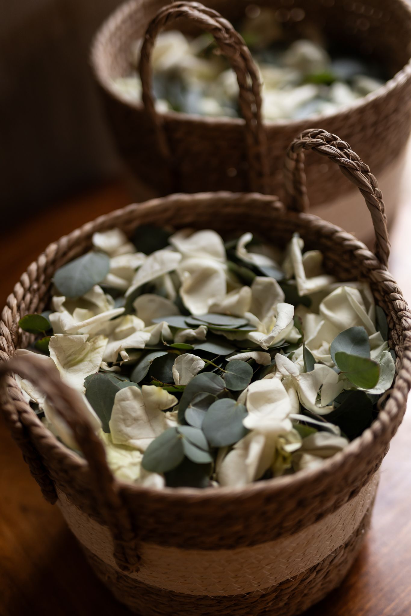 Woven basket filled with white flower petals and eucalyptus leaves for wedding ceremony.