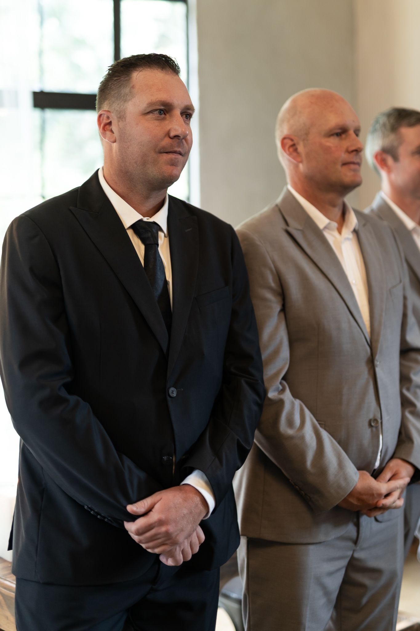 Two men in formal suits stand together at an indoor event space.