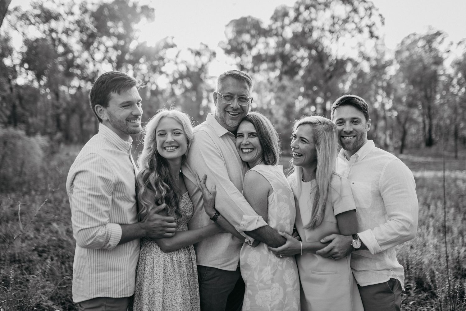 A group of people laughing and embracing outdoors during a casual photo session in a natural setting.