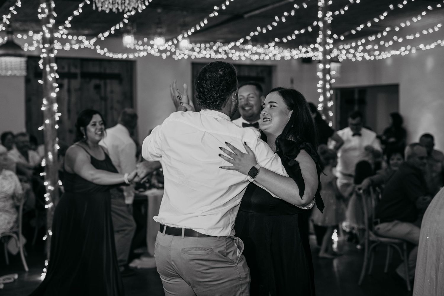 Couples dancing together at a wedding reception under twinkling string lights.