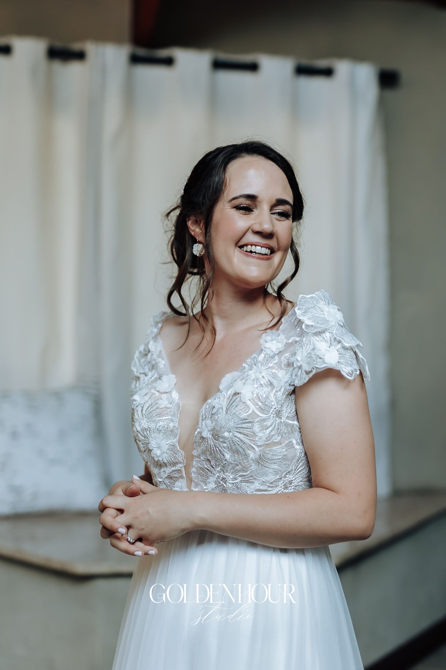 Radiant bride in floral lace cap sleeve wedding gown smiling joyfully during bridal preparations.