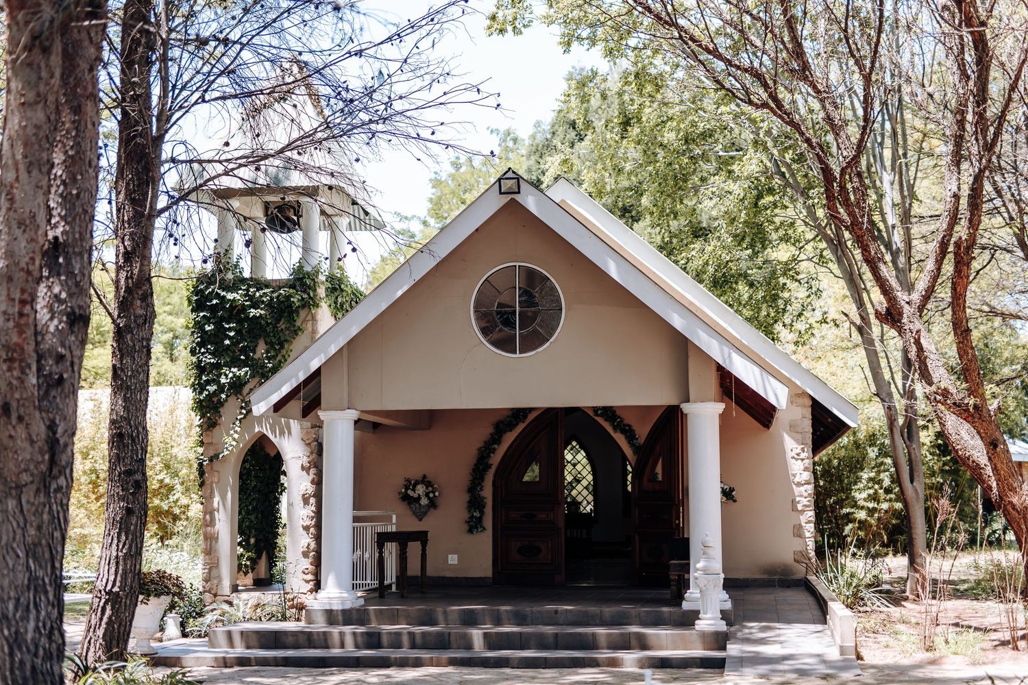 A row of small white chapel-style buildings nestled among tall pine trees in a rustic outdoor setting.