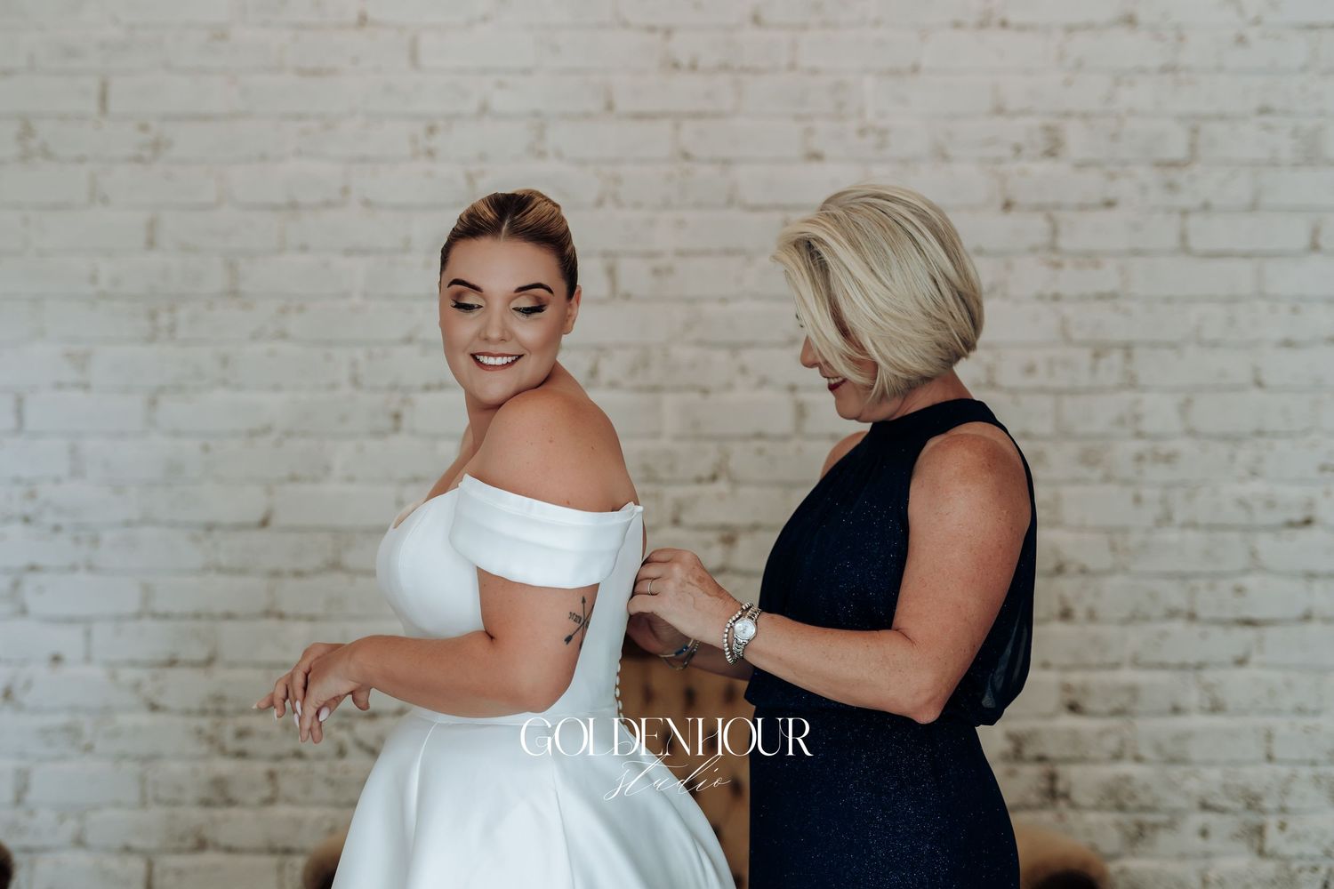 Two people in formal attire share a tender moment together against a white brick wall backdrop.